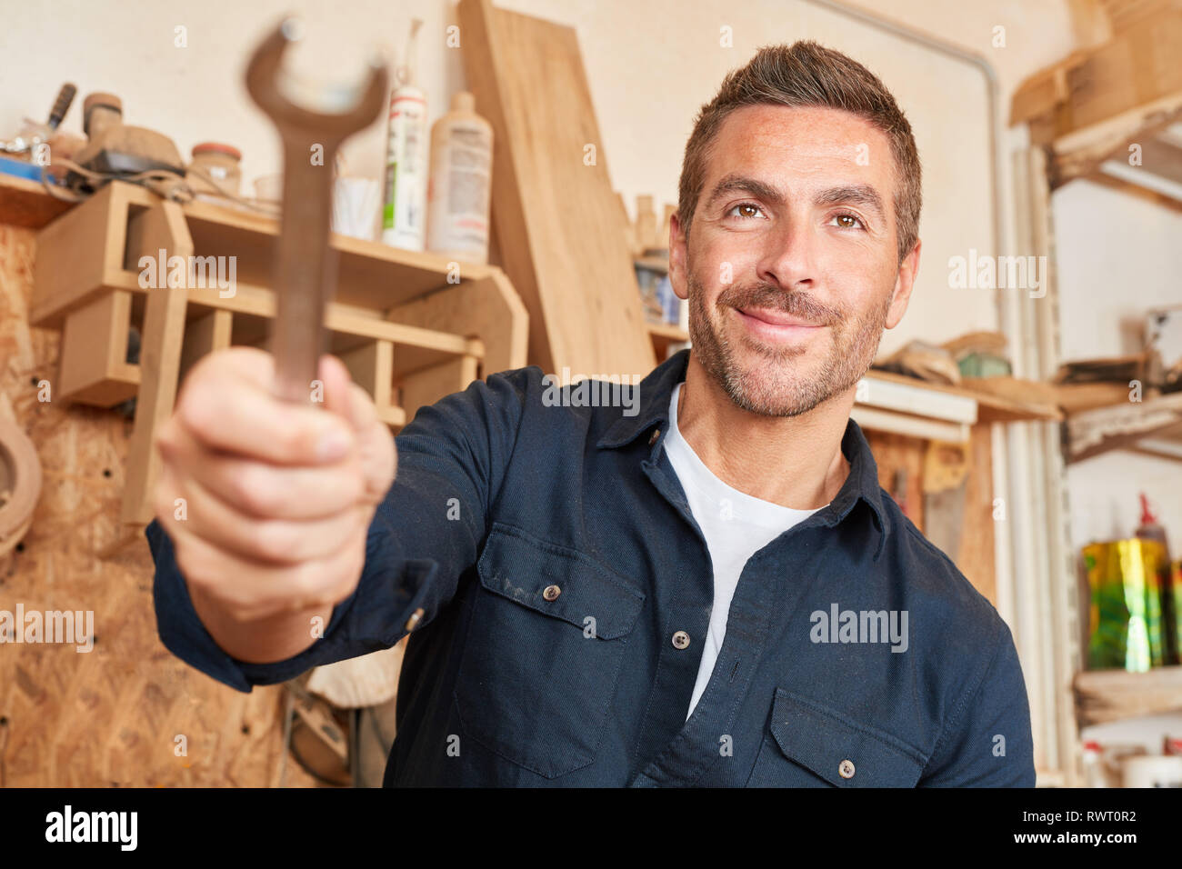 Jeune homme comme un artisan avec une clé dans son atelier de charpentier Banque D'Images