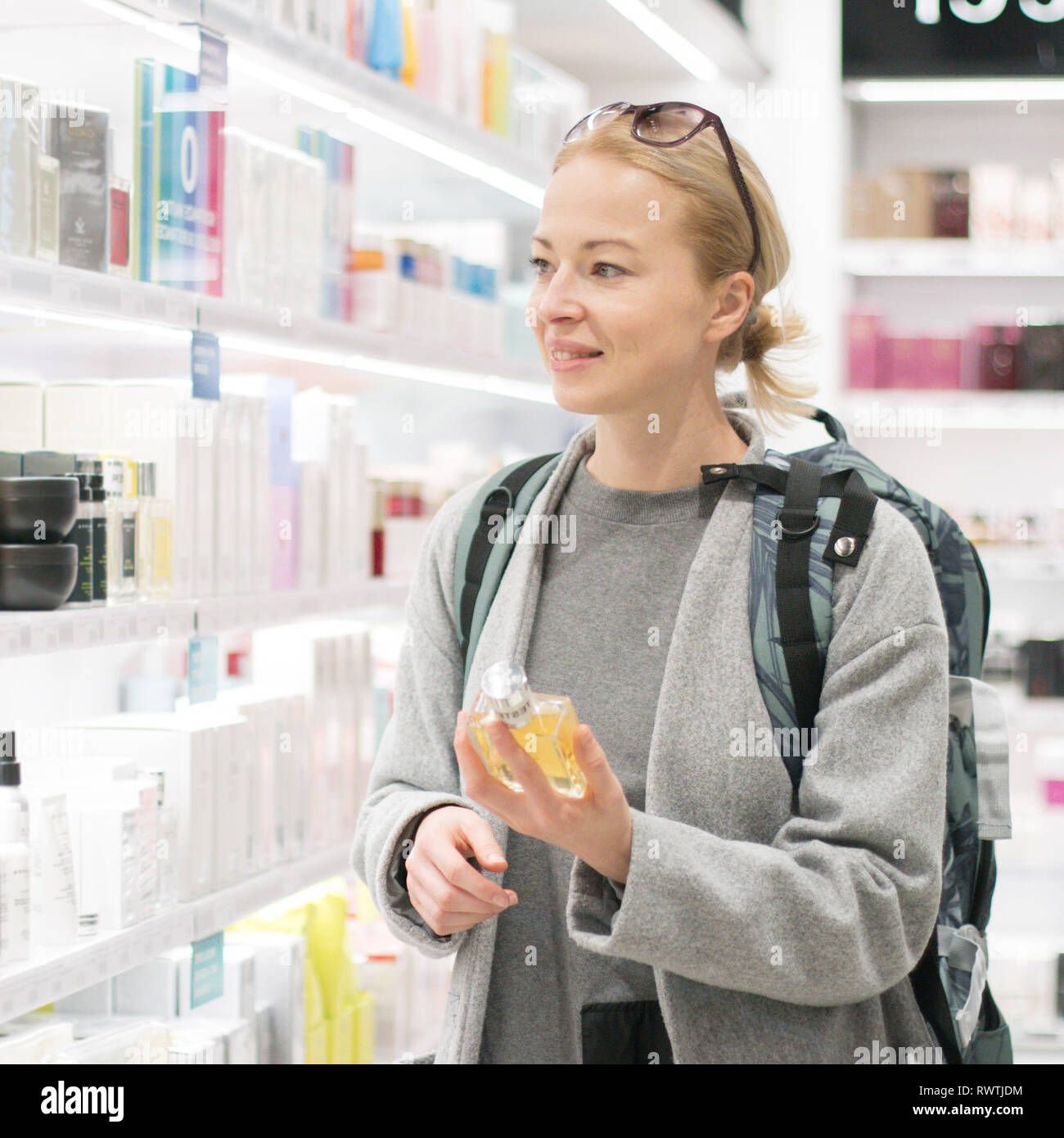 Jeune femme blonde portant des voyageurs sac à dos de voyage choisir parfum en boutique hors taxes aéroport. Banque D'Images