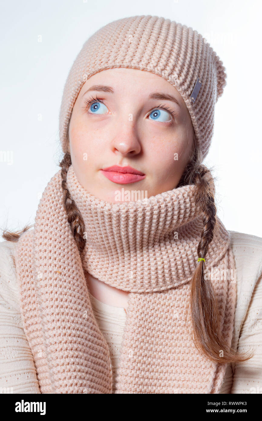 Belle jeune fille avec des yeux bleus et des tresses d'osier dans un bonnet et écharpe en tricot. Fond clair, regard mystérieux à l'autre et de haut Banque D'Images