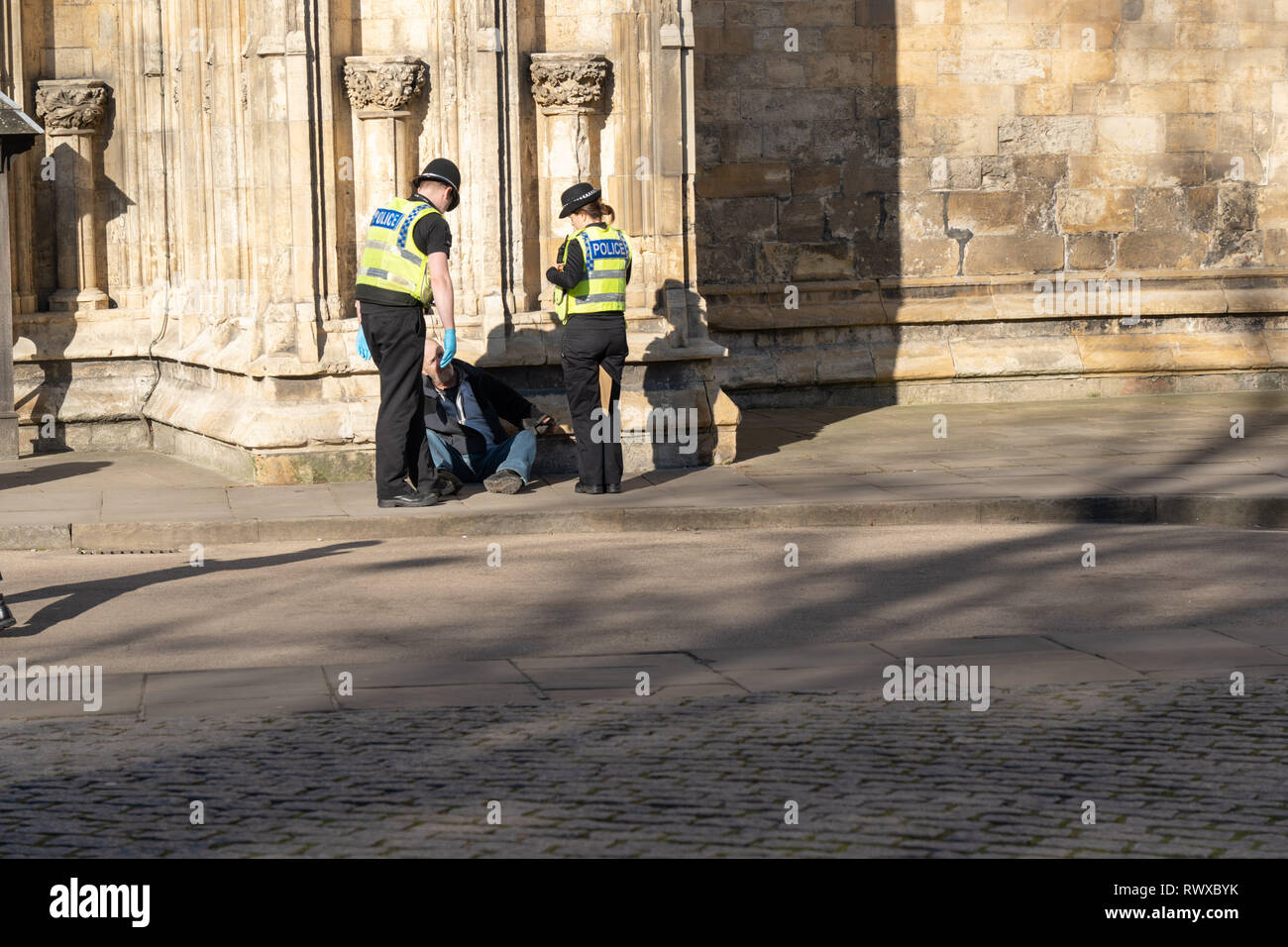 Deux agents de police fréquentant un homme se sont assis sur un trottoir à côté de York Minster, York, North Yorkshire, Angleterre, Royaume-Uni. Banque D'Images