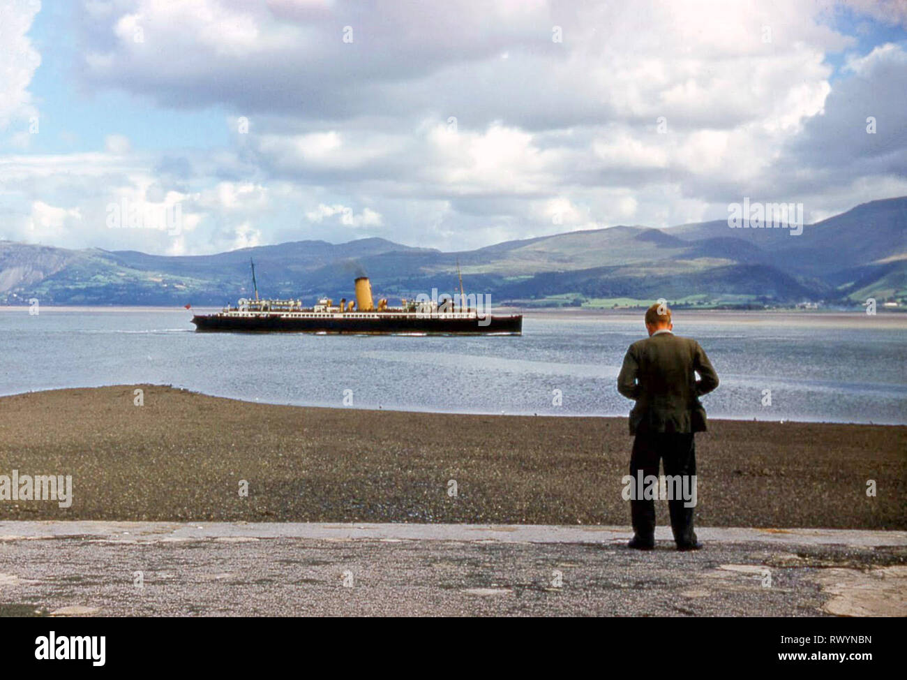 Jeune homme au niveau de la taille des photos historiques de l'appareil photo des années 60 60s vue d'archives St Tudno navire à passagers dans le détroit de Menai passant du paysage britannique Beaumaris Banque D'Images