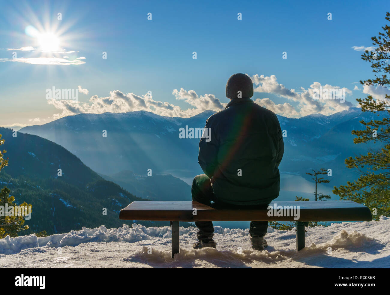 Homme assis seul sur un banc en bois, à la recherche à la belle vue montagnes. Effet arc-en-ciel sur l'homme manteau noir. Banque D'Images