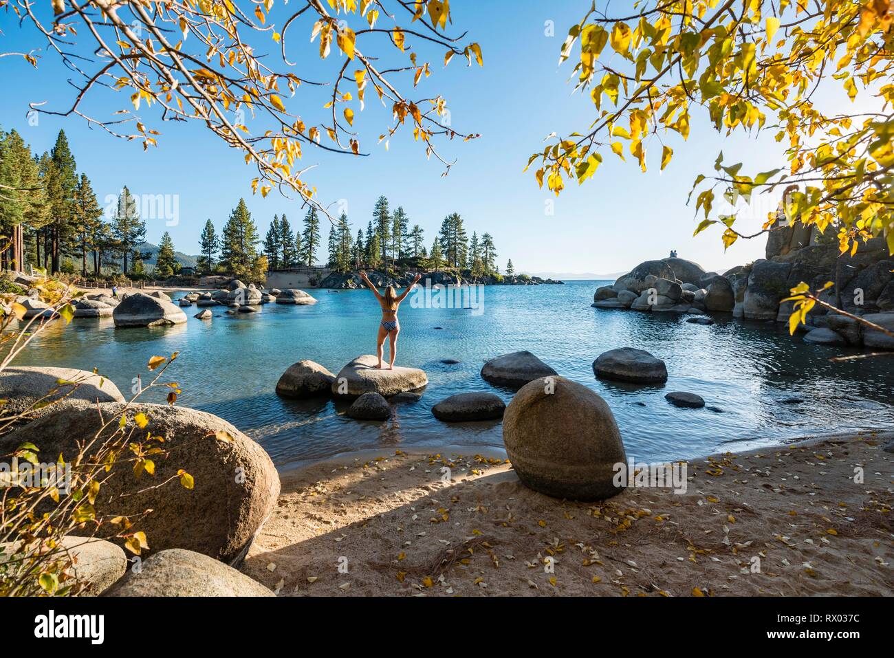 Young woman in bikini debout sur une pierre ronde dans l'eau, Bay au lac Lake Tahoe, parc d'État Sand Harbor, Port, Californie Banque D'Images