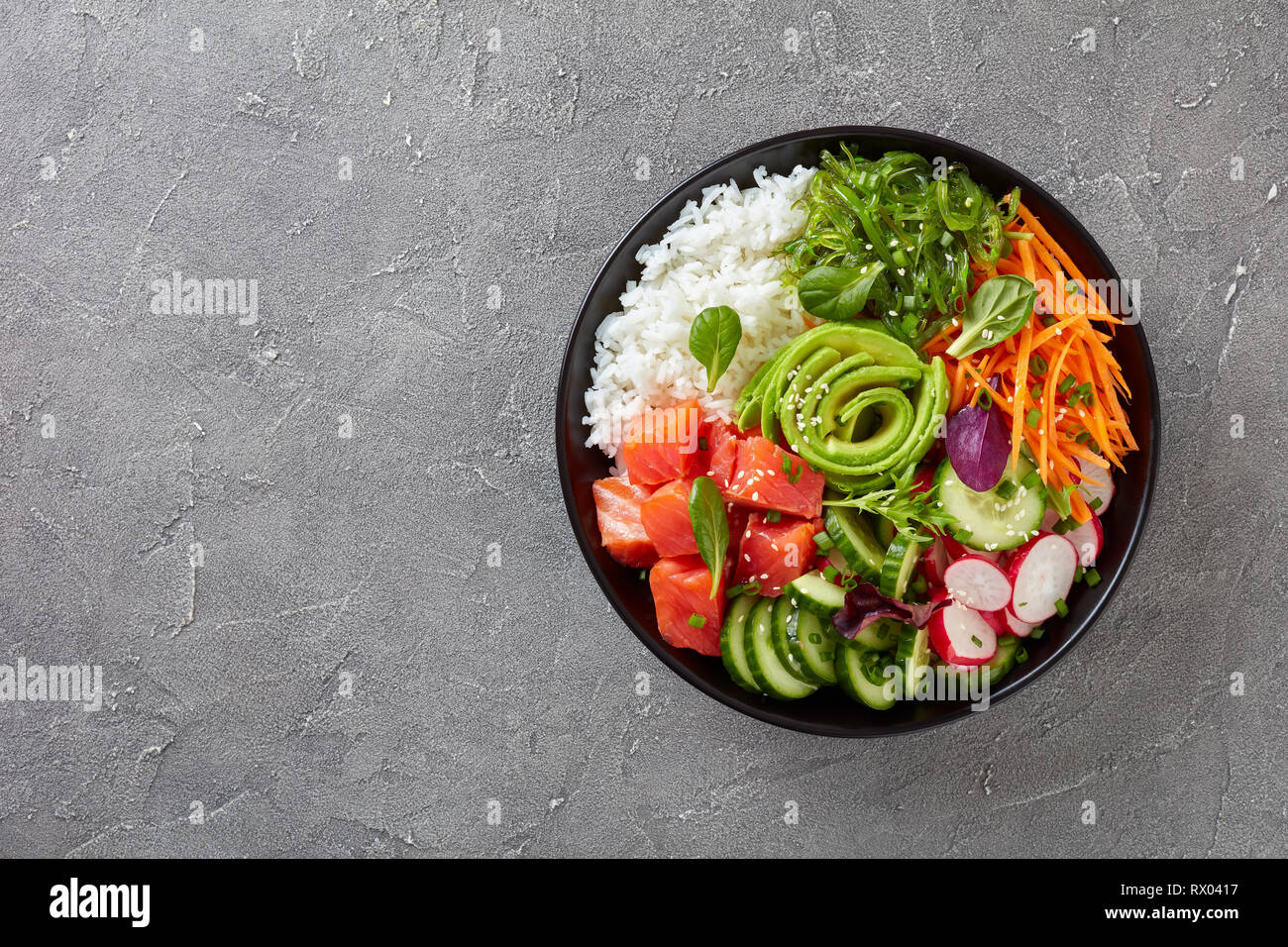 Ahi Poke saumon biologiques crus bol avec du riz, des algues, de l'avocat rose, radis, carotte, concombre et salade verte, parsemée de petits oignons et le sésame se Banque D'Images