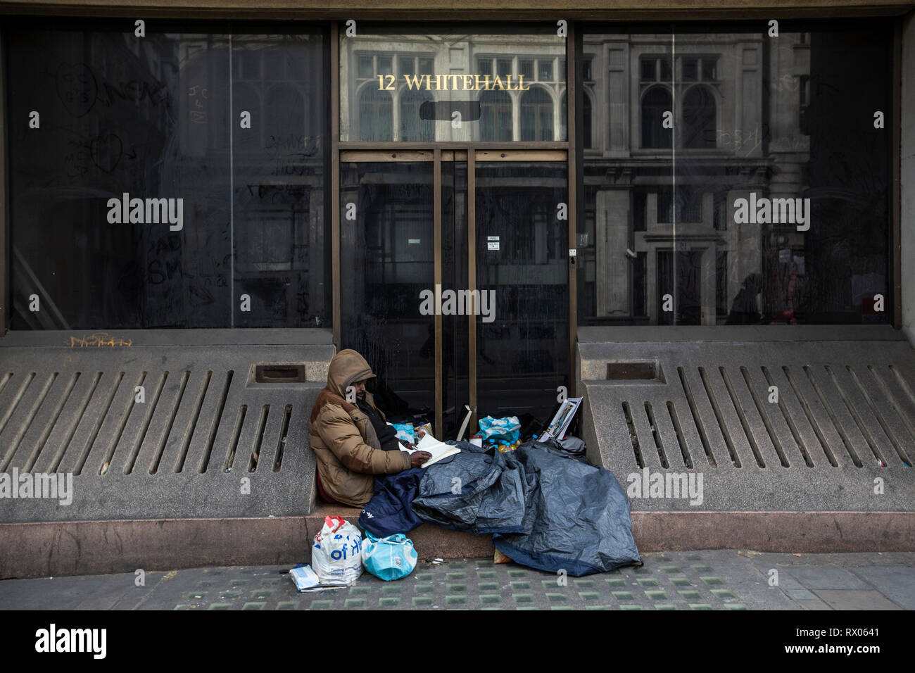 Un homme sans domicile s'est assis à écrire parmi ses biens dans une entrée du bâtiment le long de Whitehall, centre de Londres, Angleterre, Royaume-Uni Banque D'Images