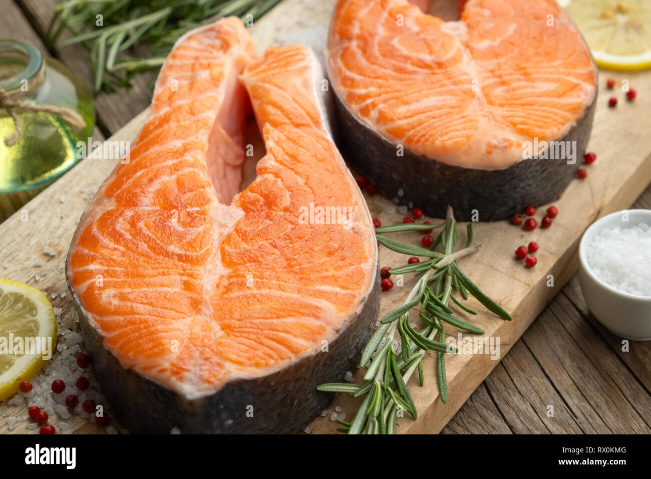 Deux darnes de saumon cru avec les tranches de citron, le sel et le romarin sur une planche à découper. Banque D'Images