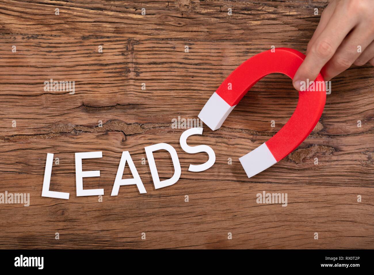 Person's Hand Holding Horseshoe aimant qui attire conduit blanc lettre sur fond de bois Banque D'Images