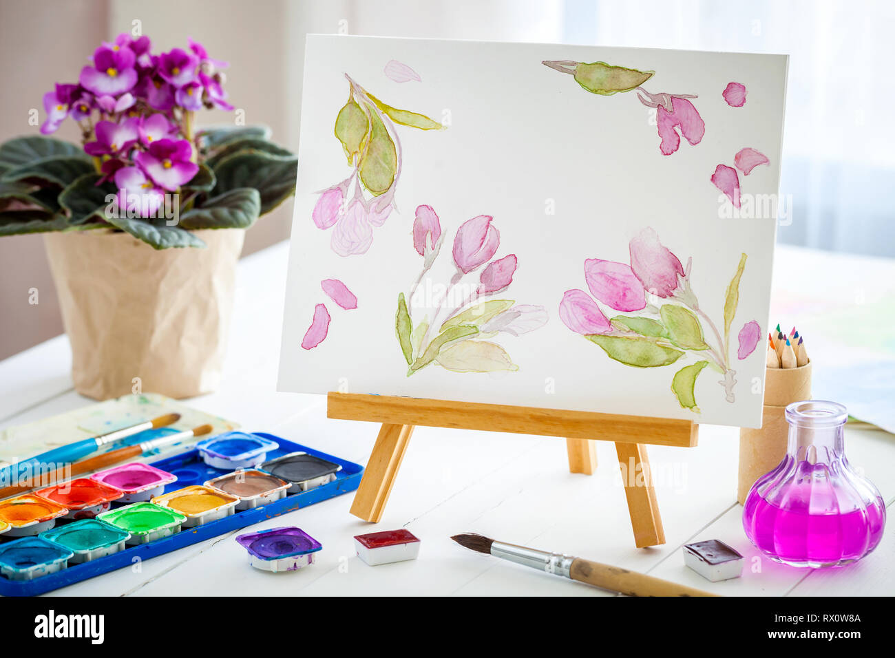 Toile sur chevalet, aquarelle, peinture, pinceaux et senpolia violet fleur en pot. Banque D'Images
