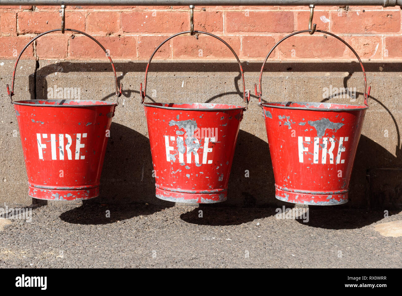 Trois rouges vieux seaux d'incendie vintage pendaison sur crochets à Maldon railway station, Victoria, Australie. Banque D'Images
