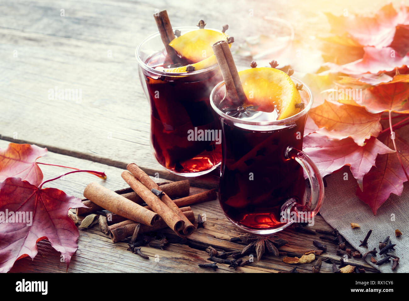 Tasses en verre de vin chaud avec des épices et orange agrumes sur table en bois avec des feuilles d'érable. Banque D'Images