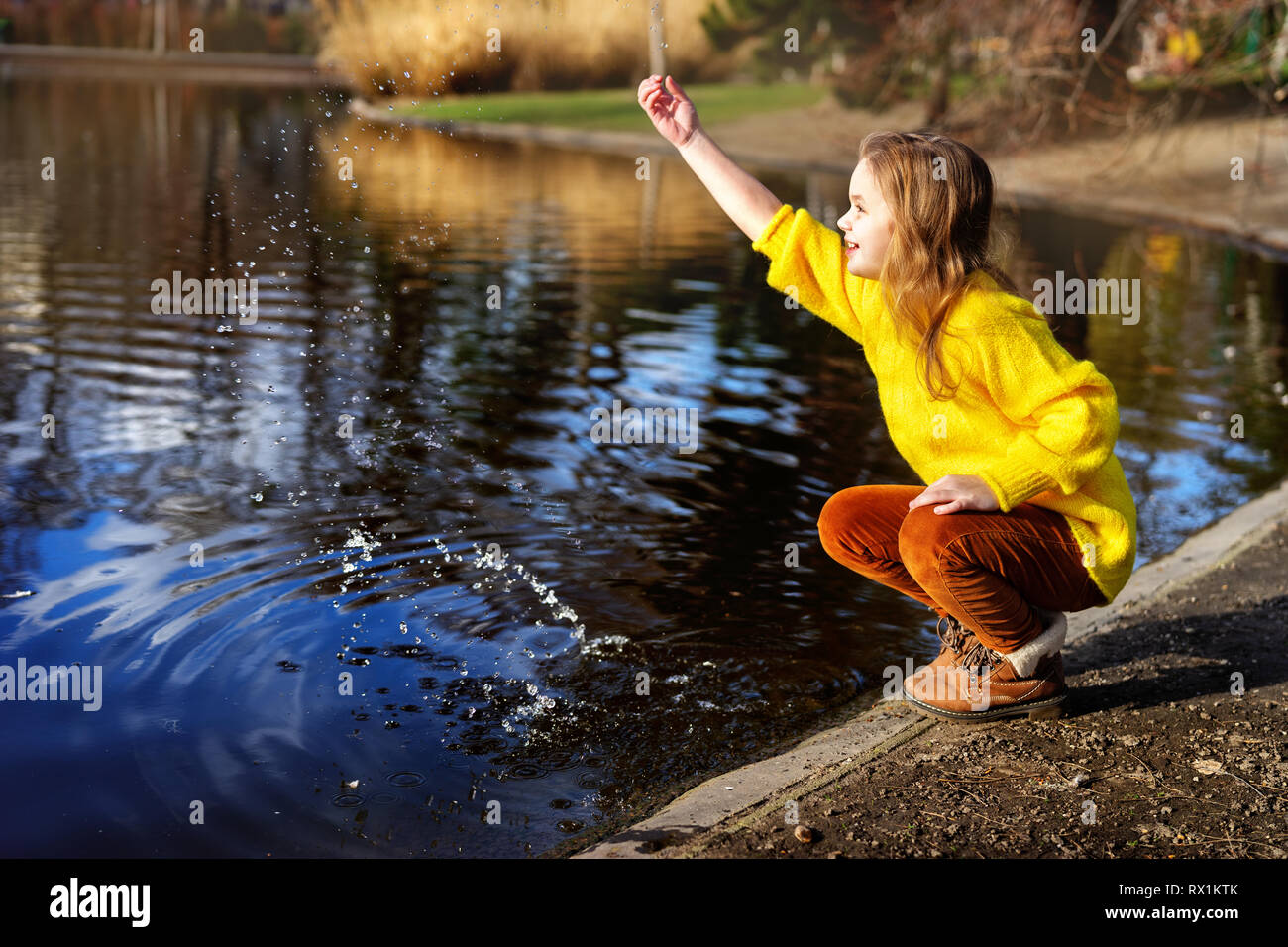 Heureux l'enfant fille en pull jaune vif de payer avec de l'eau dans la nature Banque D'Images