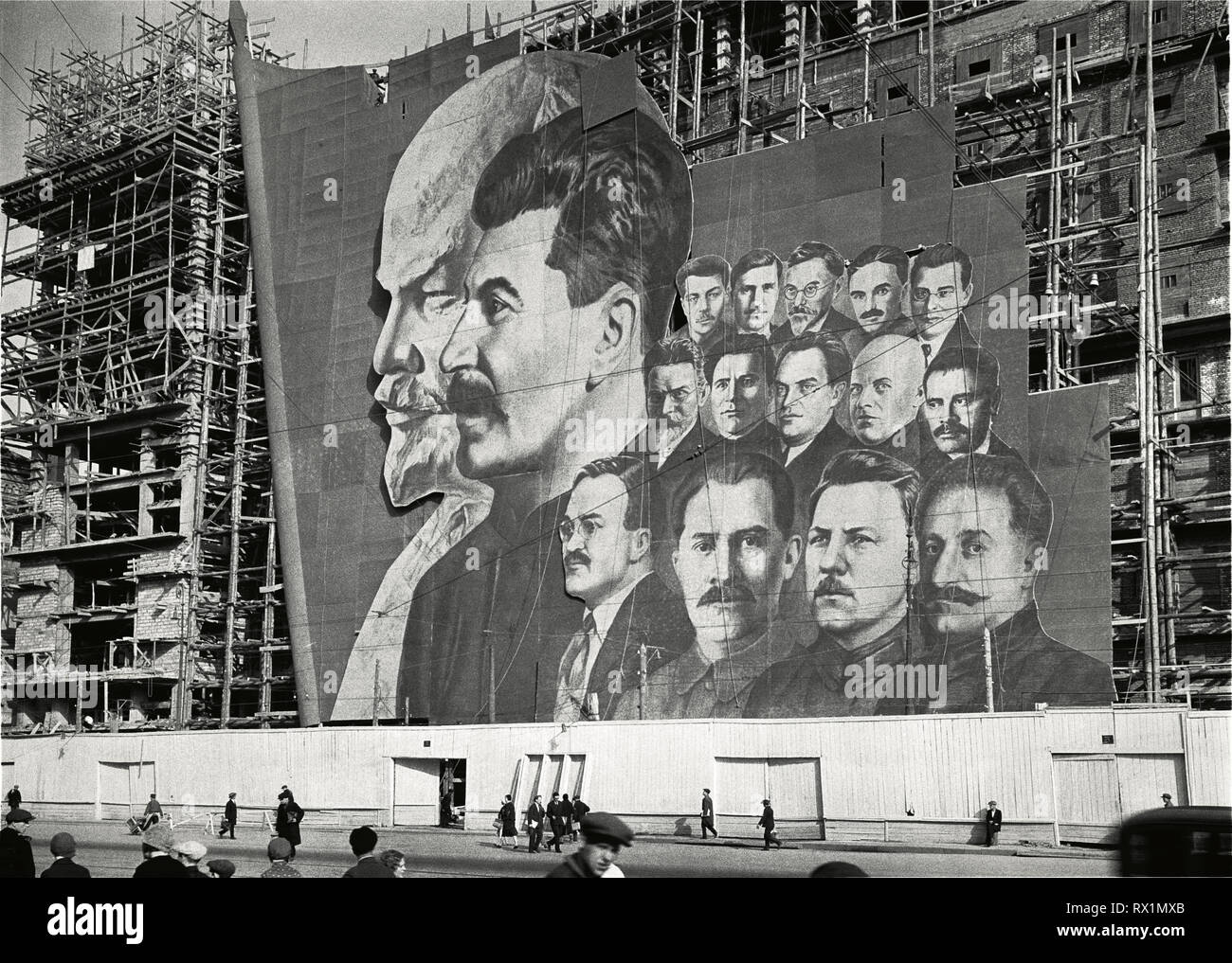 Une grande affiche avec des portraits des dirigeants politiques russes Vladimir Lénine, Joseph Staline et d'autres pour la parade du jour de mai pend sur l'échafaudage d'un bâtiment en construction, Moscou, Russie, 1934.(Photo de Burton Holmes) Banque D'Images