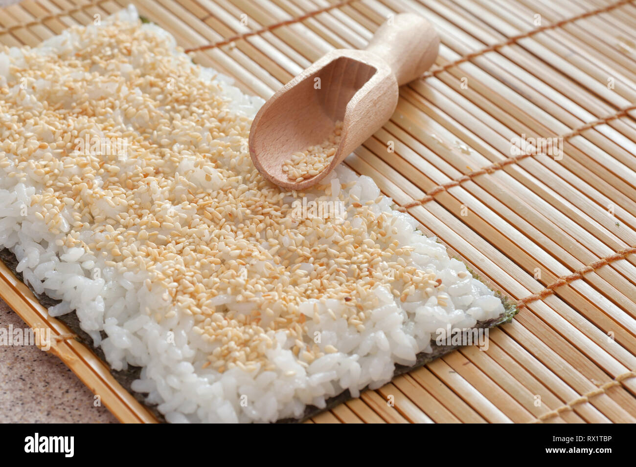 Préparation de sushi. Nori avec du riz et des graines de sésame sur le tapis de bambou. Banque D'Images