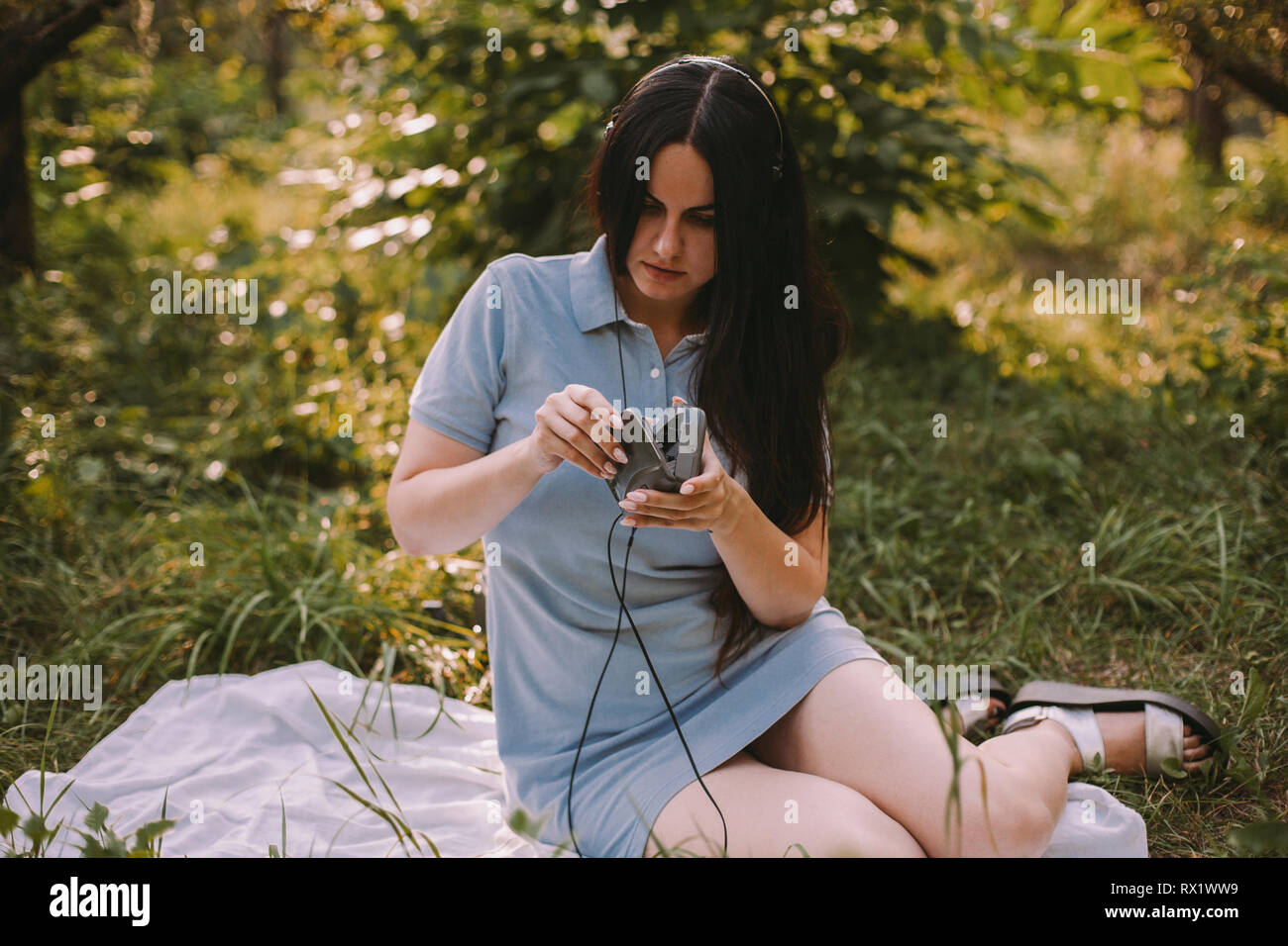 Femme avec de longs cheveux listening music while sitting on grassy field in garden Banque D'Images