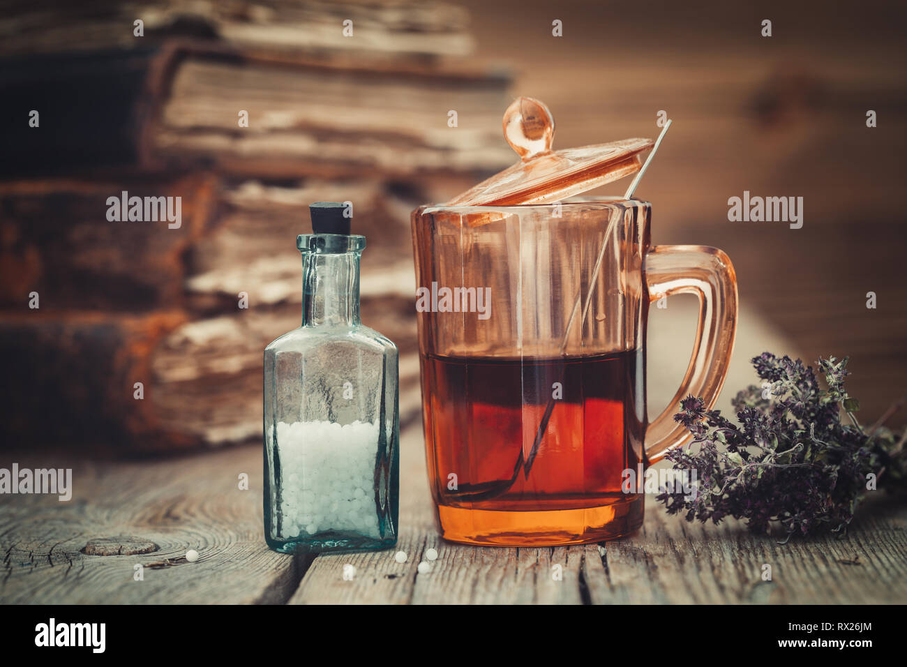 Teinture ou de thé en bonne santé dans le verre, flacon de globules homéopathiques, de vieux livres et de tas d'herbes sèches en bonne santé. Banque D'Images