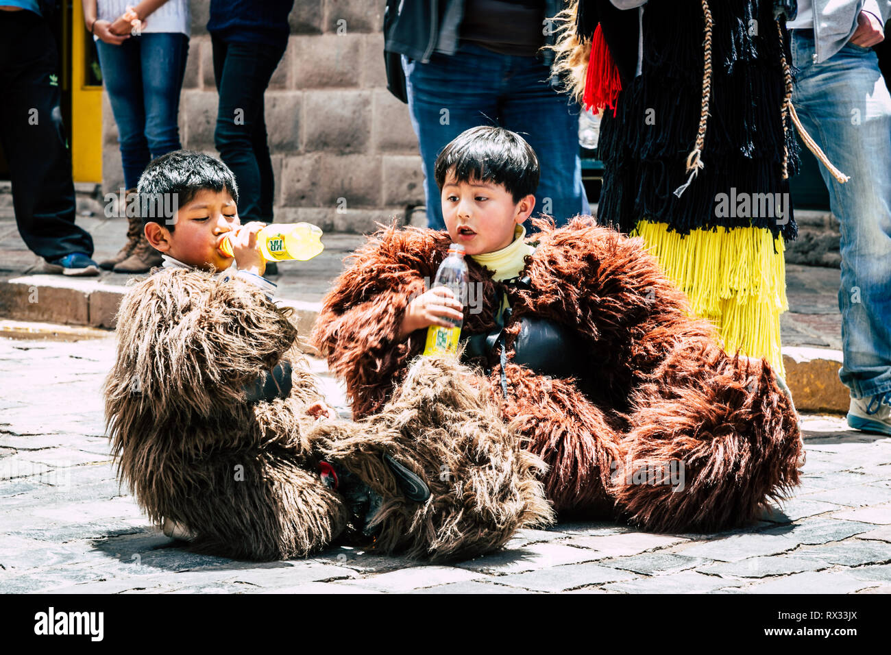 Deux garçons assis sur la rue portant des costumes d'ours soude potable sur une chaude journée ensoleillée. Un garçon de boire pendant que l'autre lui montres surpris. Banque D'Images