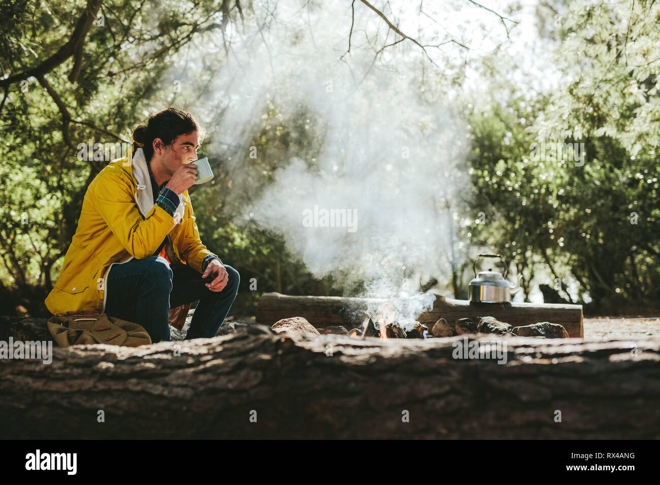 Homme appréciant une tasse de thé assis à côté d'un feu de camp dans une forêt. voyageur sur un voyage d'aventure dans la campagne assis près d'un feu de joie buvant du thé. Banque D'Images