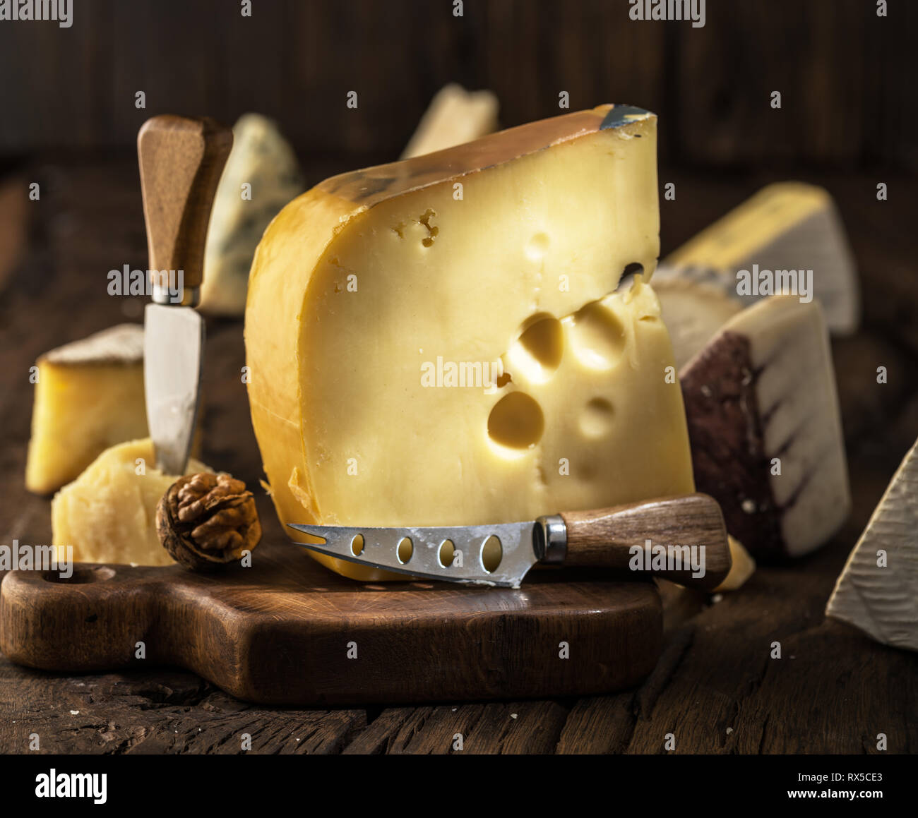 Morceau de fromage Maasdam du lait de vache sur planche de bois. Gamme de fromages à l'arrière-plan. Banque D'Images