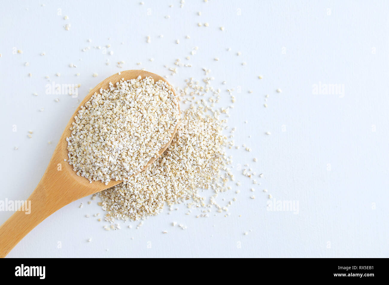 Le gruau d'orge sur une cuillère en bois et la diffusion. Arrière-plan blanc. Banque D'Images