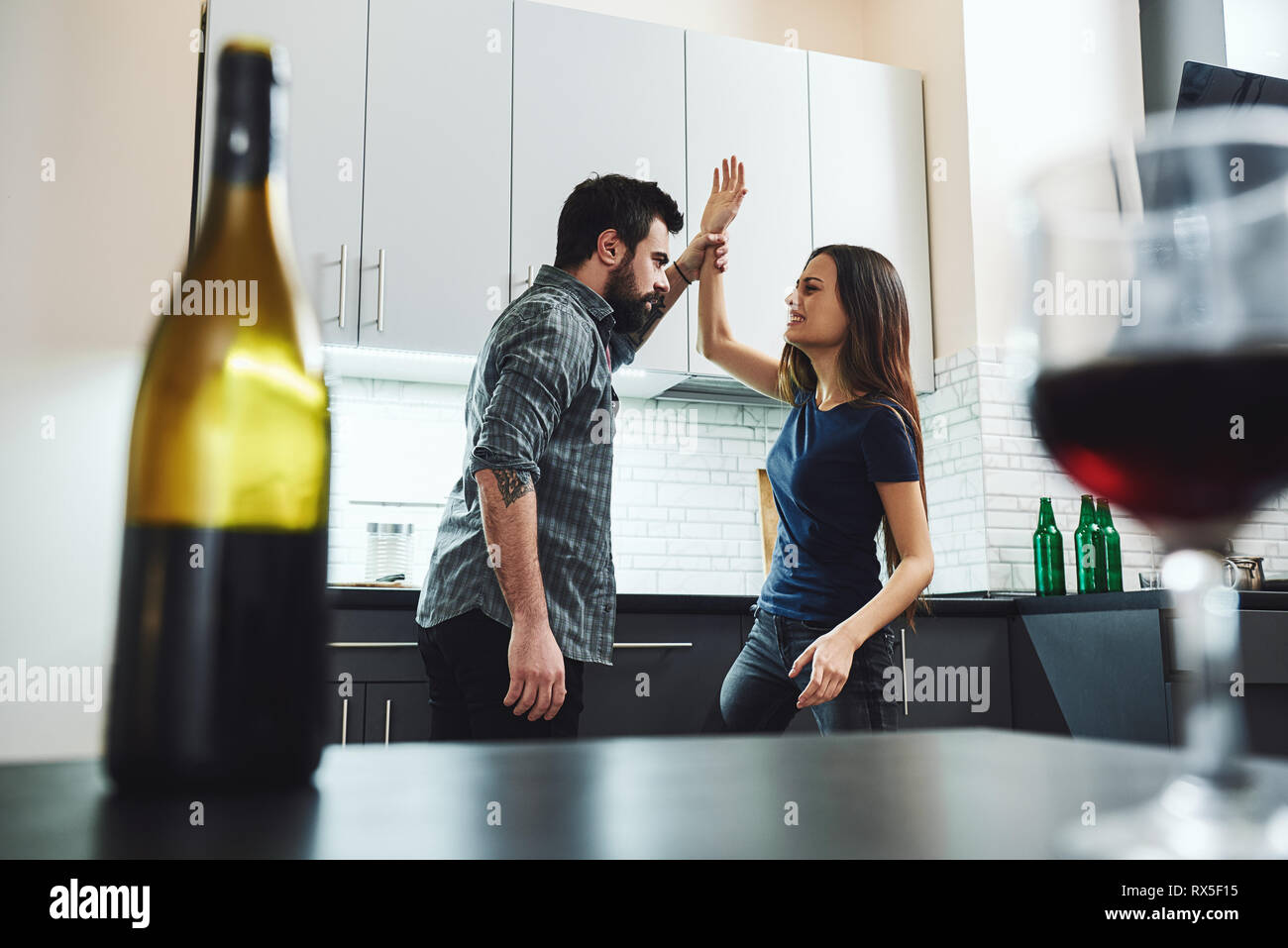 Portrait of man and woman having argument, combats dans la cuisine. Une bouteille et un verre de vin sont sur la table. Selective focus Banque D'Images