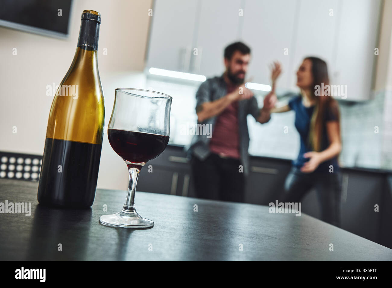 Portrait of man and woman having argument, debout dans la cuisine. Une bouteille et un verre de vin sont sur la table. Selective focus Banque D'Images