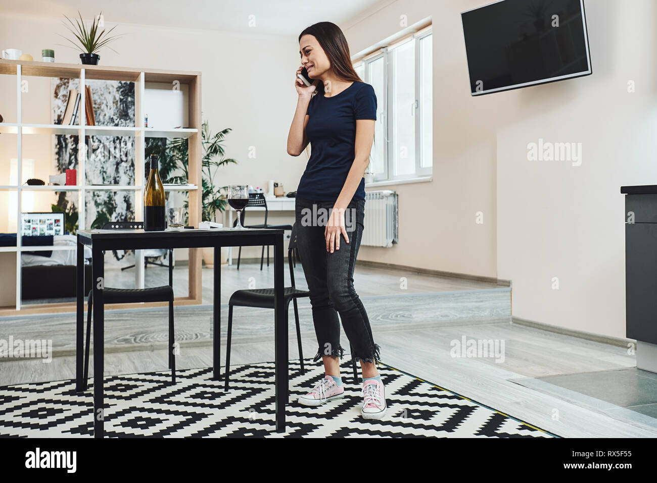 Dark-haired, triste et perdu femme alcoolique debout dans la cuisine, à parler au téléphone à la maison. Elle est complètement ivre, à la dépression, la solitude Banque D'Images