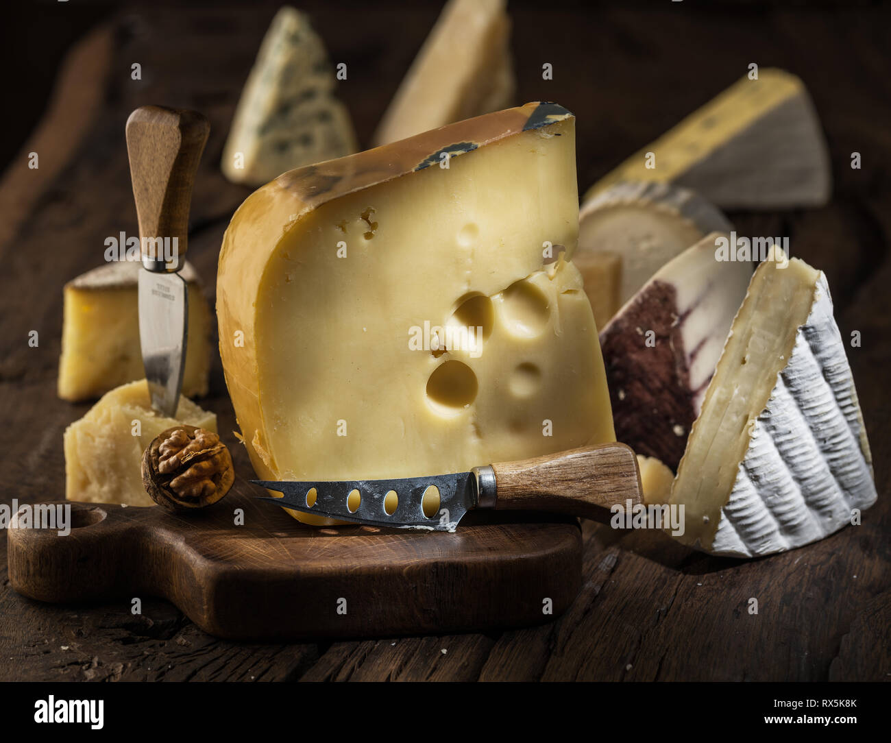 Morceau de fromage Maasdam du lait de vache sur planche de bois. Gamme de fromages à l'arrière-plan. Banque D'Images