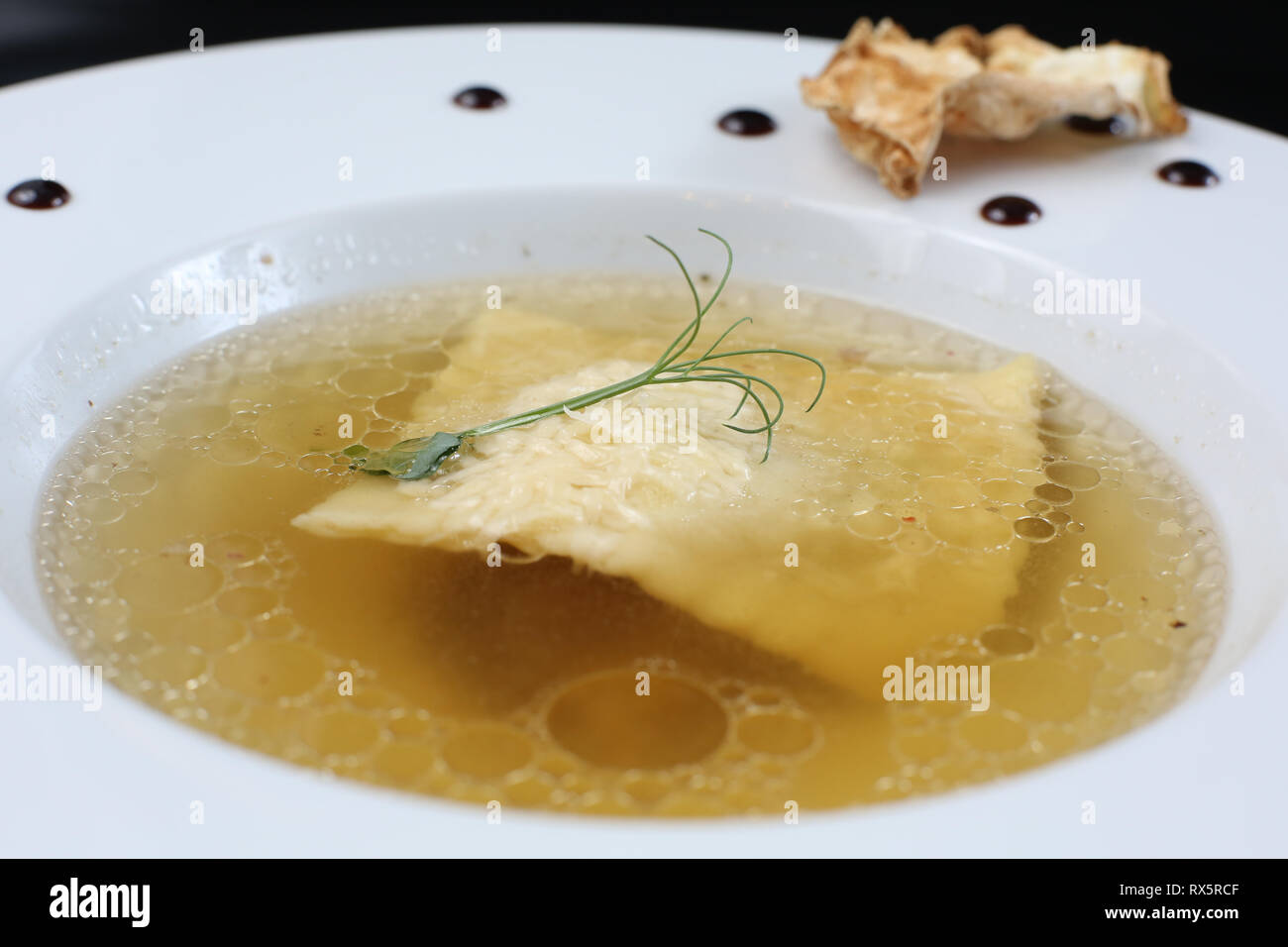 Service de restauration, minimaliste blanc transparent le bouillon de poulet dans une assiette de riz, fromage et de raviolis, décoré de germe de pois Banque D'Images