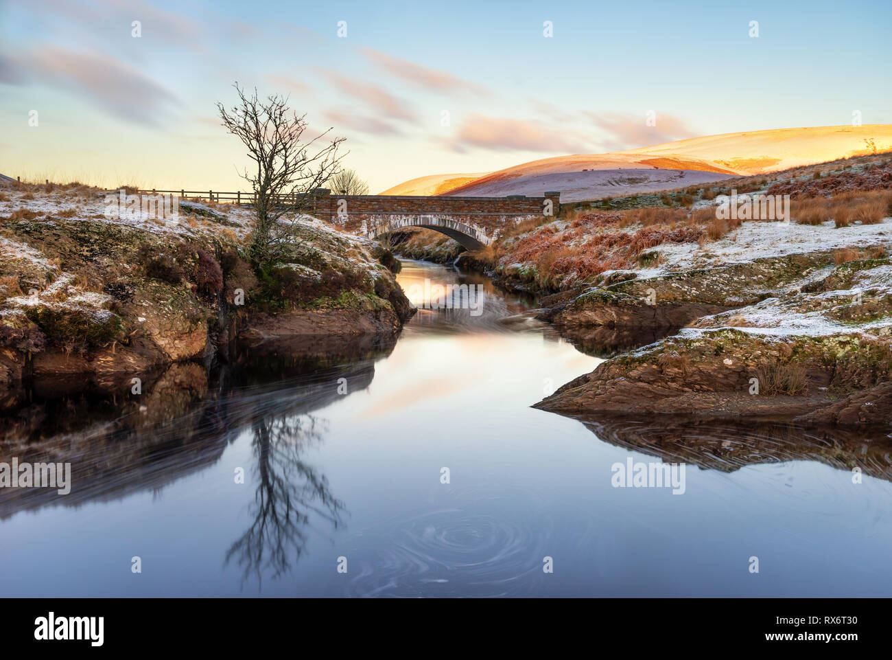 Pont AR, Elan Elan Valey, galles scène enneigée d'Afon Elan qui passe par un pont en hiver avec Lone Tree reflétée dans l'eau et soleil du matin li Banque D'Images