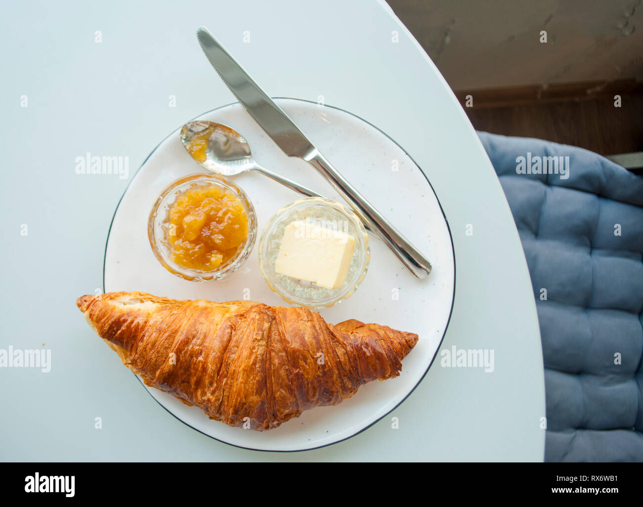 Croissant frais avec de la confiture, du beurre et du cappuccino avec belle latte art sur table gris dans un café. Mise à plat d'un petit-déjeuner frais. Banque D'Images