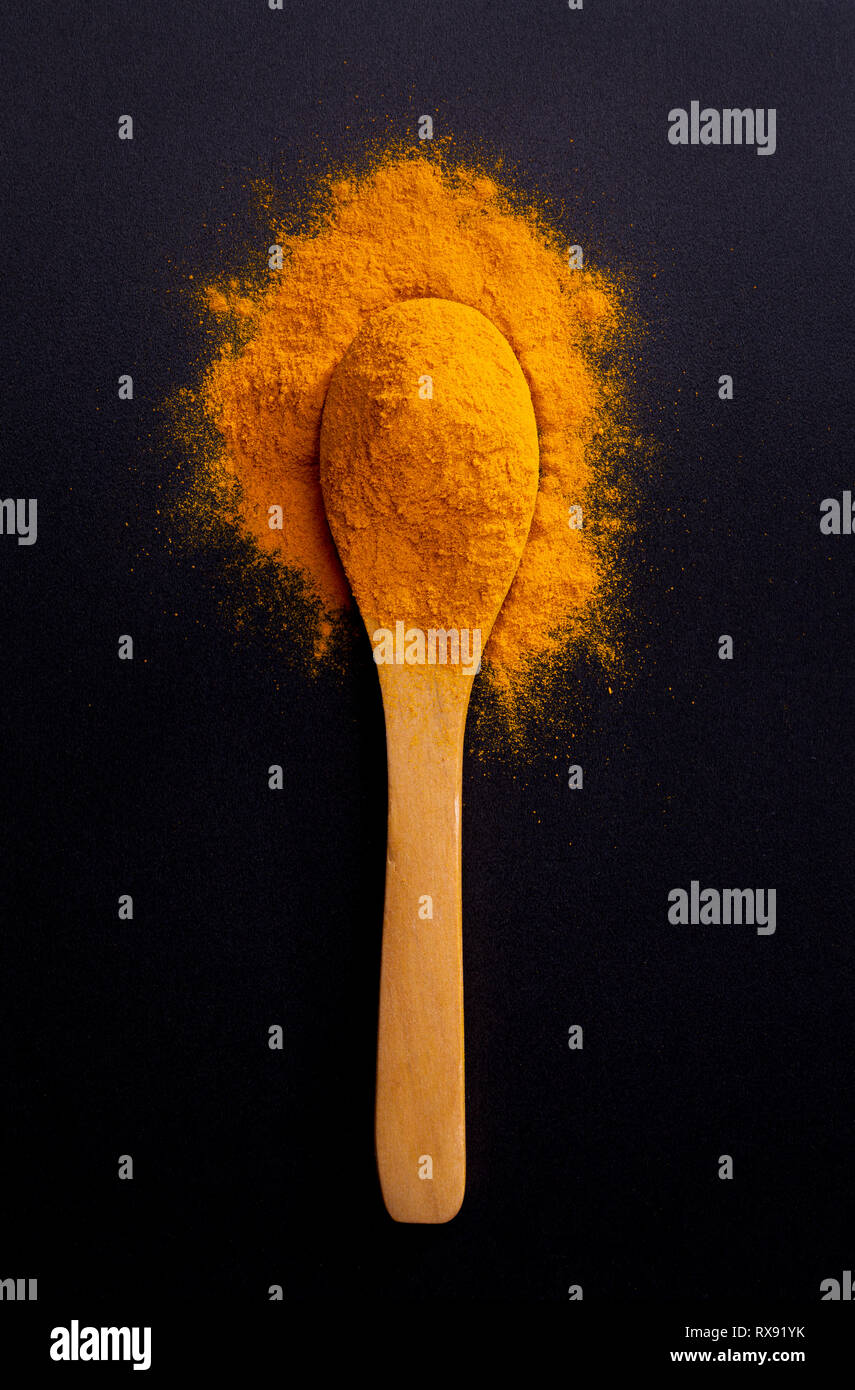 Des tas d'épices curcuma curcuma sur cuillère en bois sombre sur fond noir, vue du dessus Banque D'Images