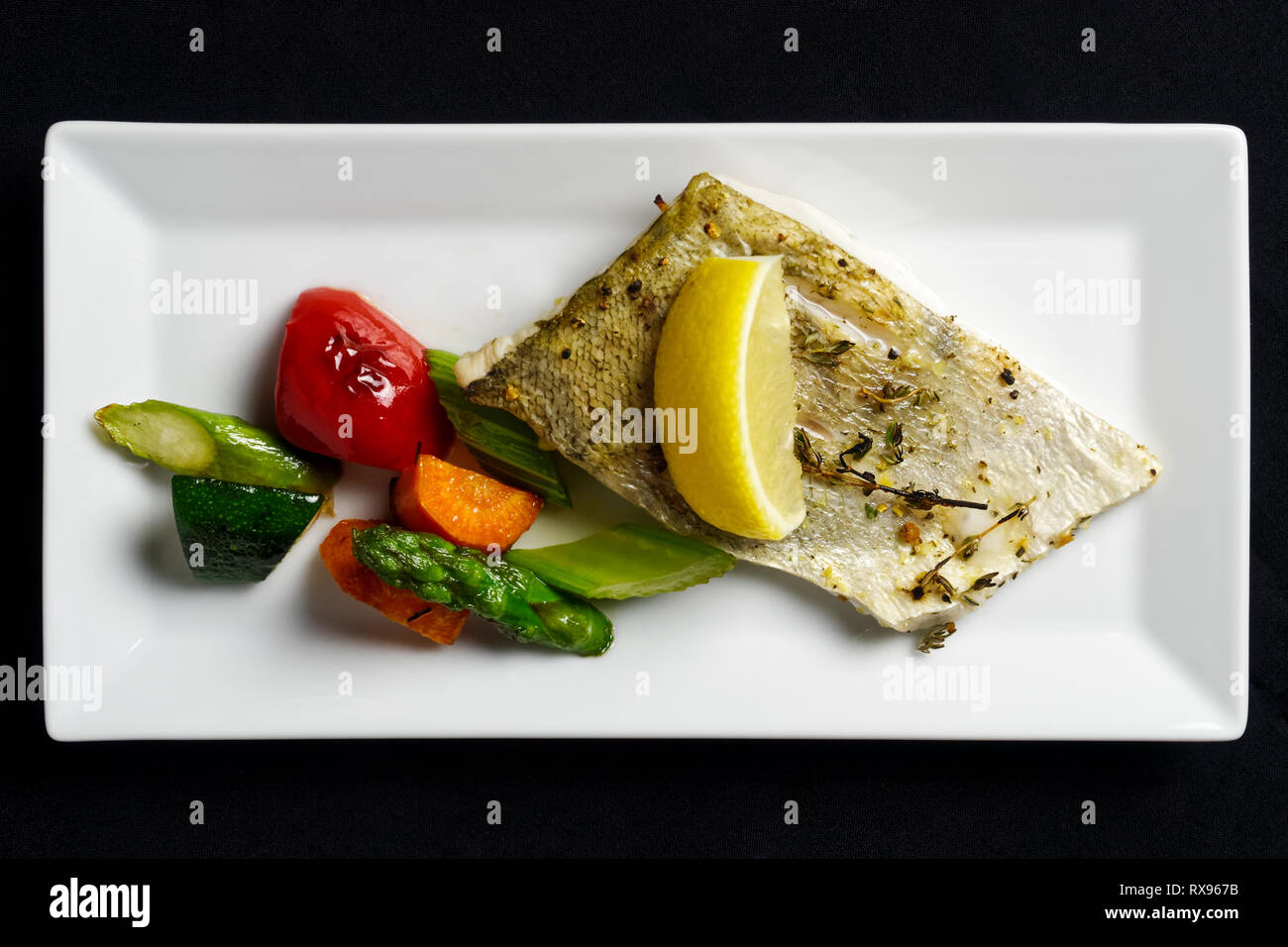 Filet de sandre grillé avec des légumes grillés sur la plaque rectangulaire blanc à partir de ci-dessus. Fond noir. Banque D'Images