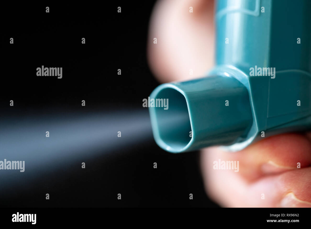 Hand holding blue asthme inhalateur avec spray sortir sur fond noir. Banque D'Images