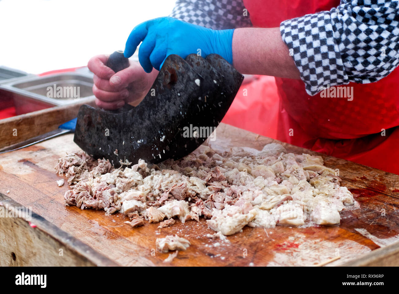 Un homme couper la viande avec une planche de bois sur mezzaluna traditionnel lors de l'Abattage des porcins. À l'extérieur. Banque D'Images