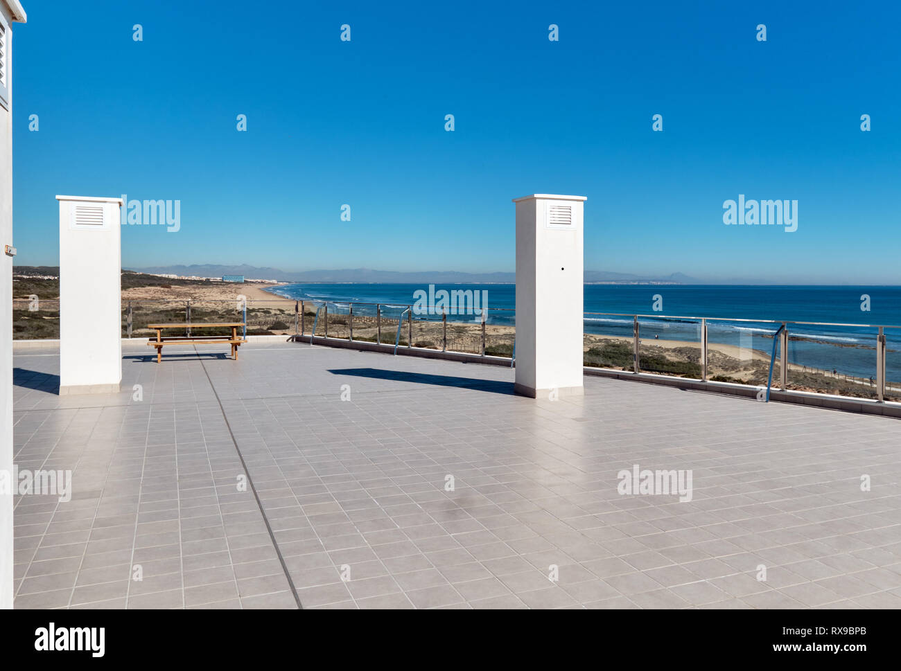 Terrasse spacieuse carrelée parquet gris vide verre transparent limite de clôture et seul banc avec vue magnifique sur la mer Méditerranée, bleu clair Banque D'Images