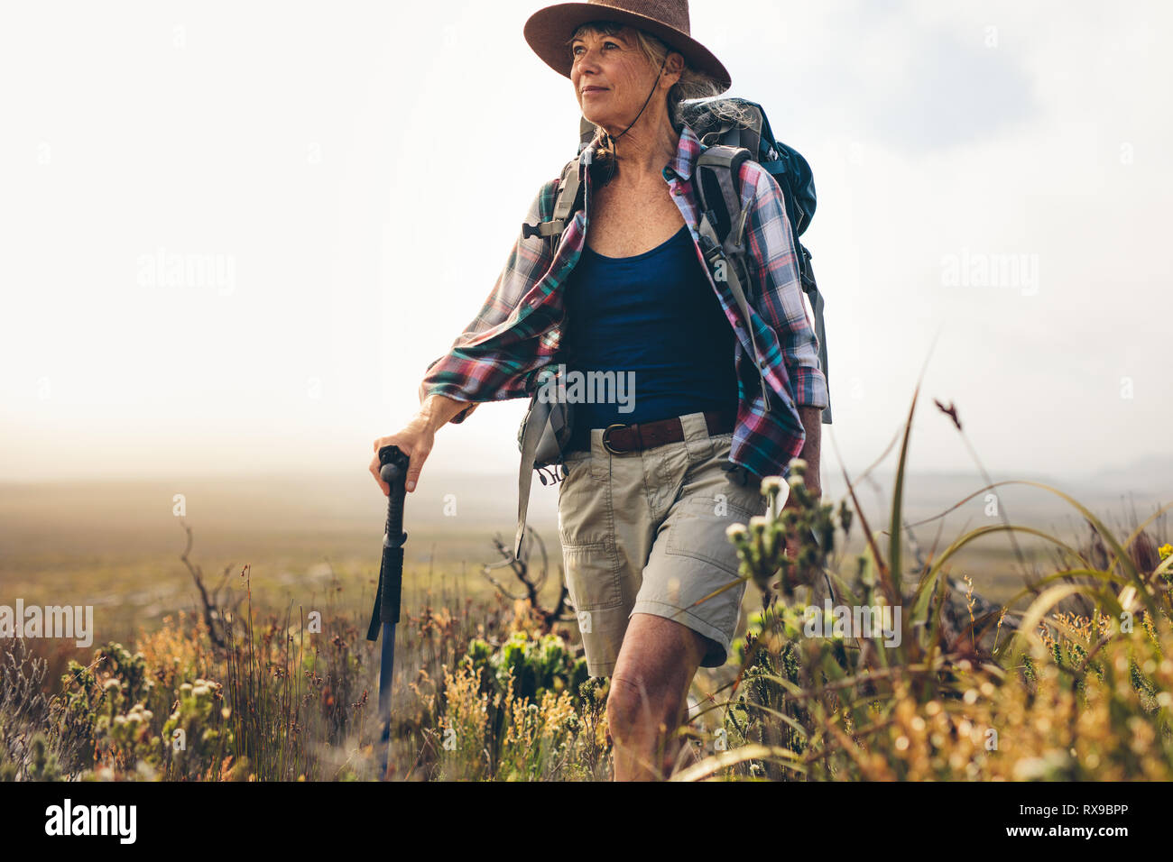 Femme aventureux sur un sentier de randonnée sur une journée nuageuse. Senior woman wearing hat et son sac à dos de trekking dans la campagne tenant un pôle randonnée. Banque D'Images