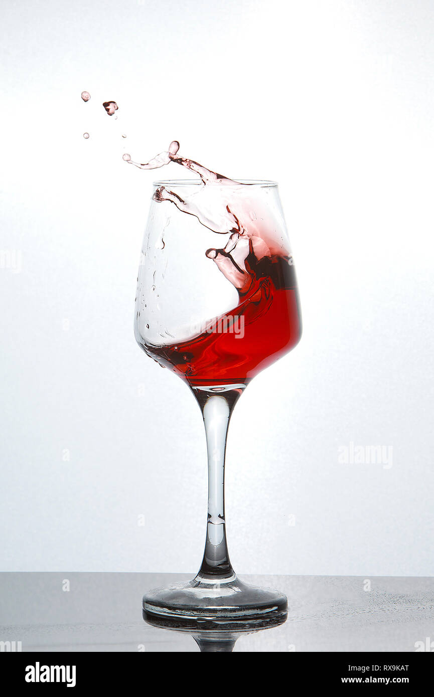 Close-up of red wine splashing in glass on table sur fond blanc Banque D'Images