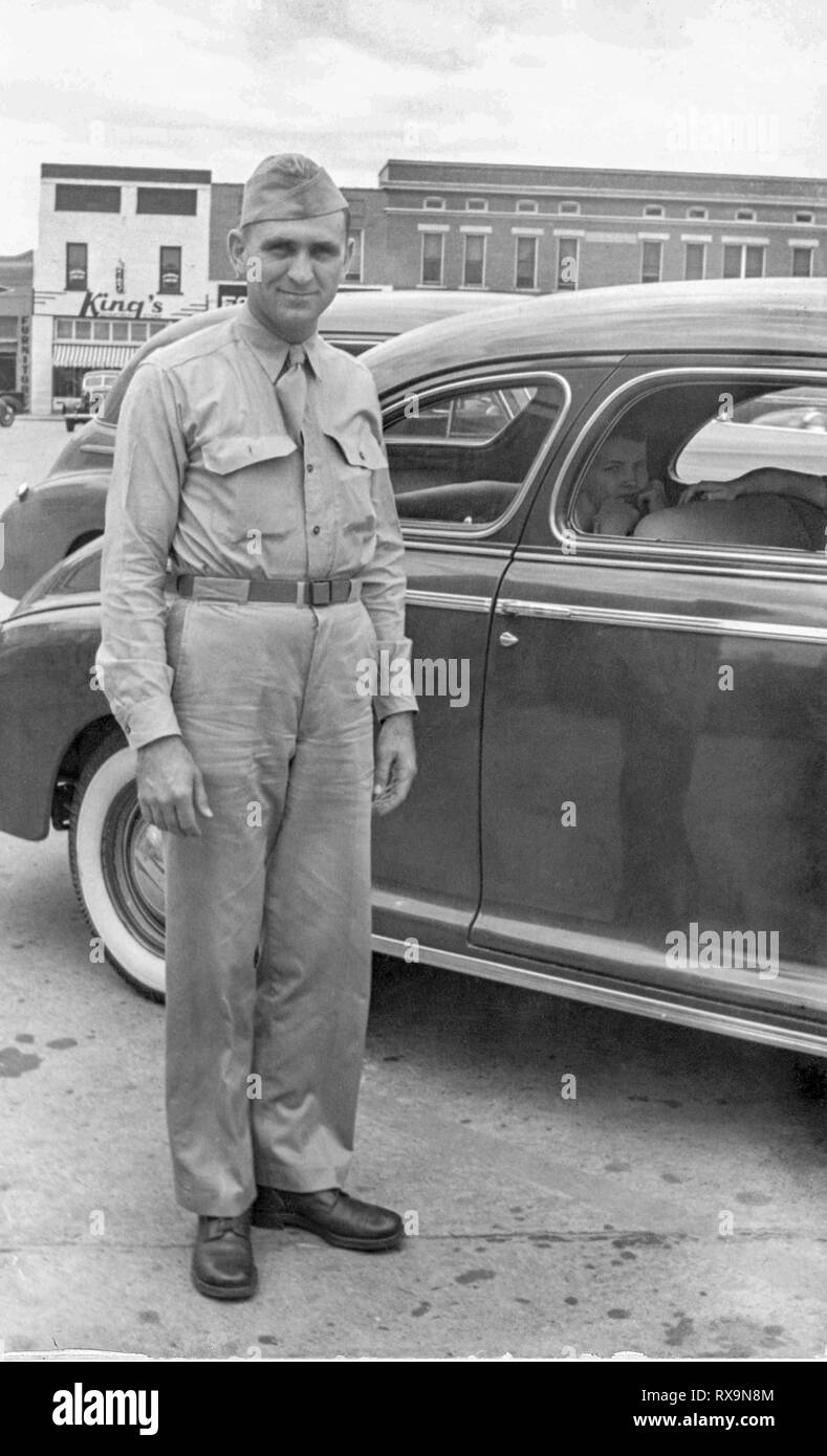Shot verticale de jeune soldat américain en uniforme debout à côté d'une voiture juste avant le déploiement en Europe. Ancien numérisé d'une photo de famille. Peut contai Banque D'Images