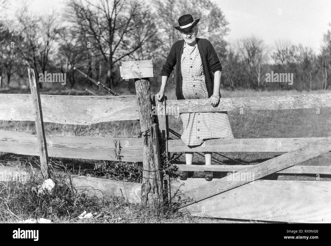 Horizontal noir et blanc d'une vieille dame l'ascension d'une clôture avec ses cannes à pêche au début des années 1900. Ancien numérisé d'une photo de famille. Peut conta Banque D'Images