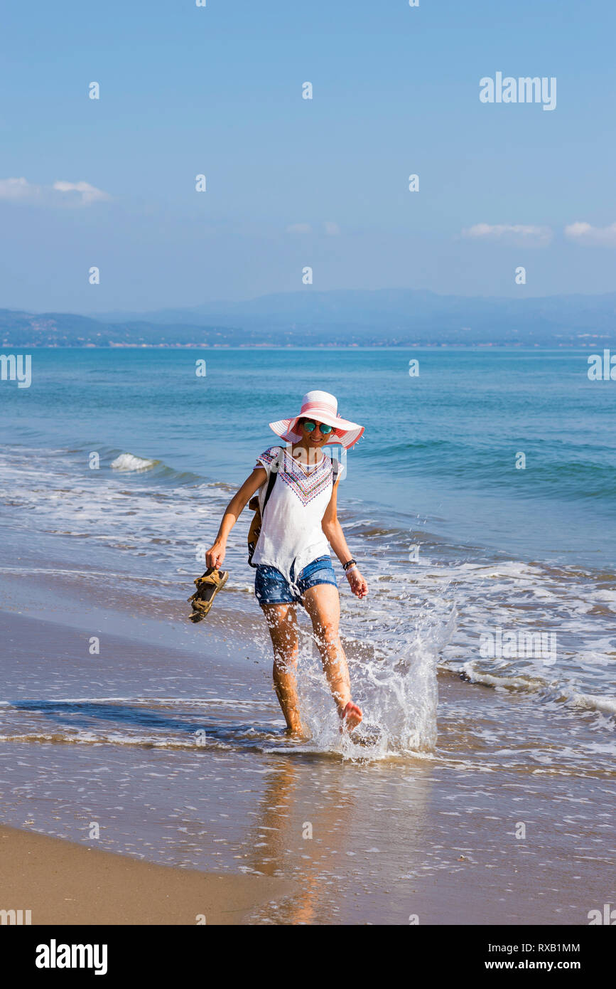 Happy woman splashing water at shore contre le ciel bleu au cours de journée ensoleillée Banque D'Images