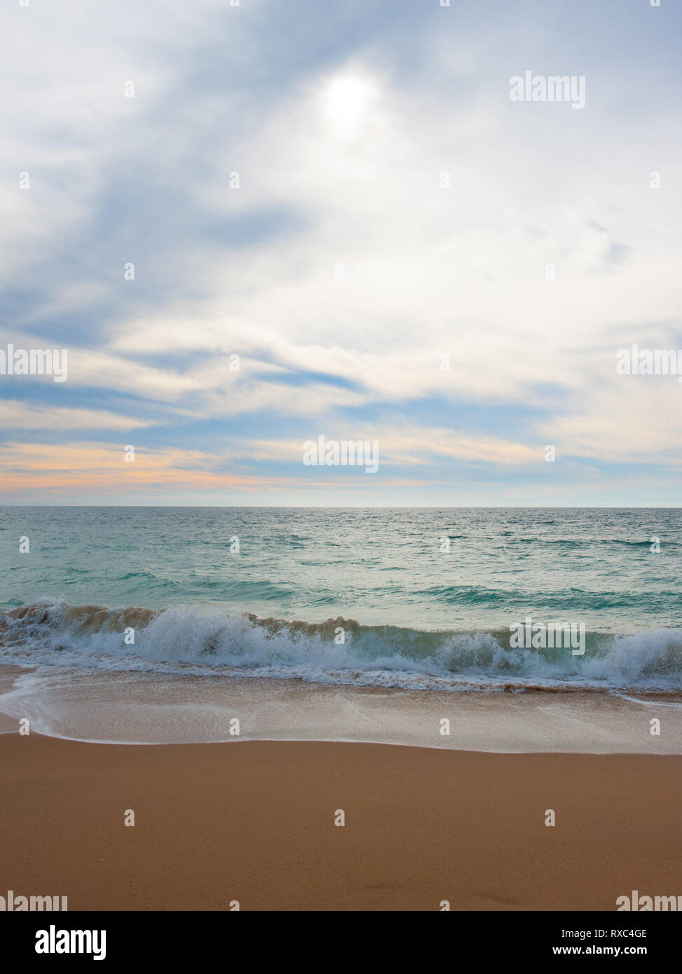 Seascape pacifiques avec des vagues léchant doucement le rivage sur le sable. Soleil eau filtre à travers les nuages couvrant le ciel Banque D'Images