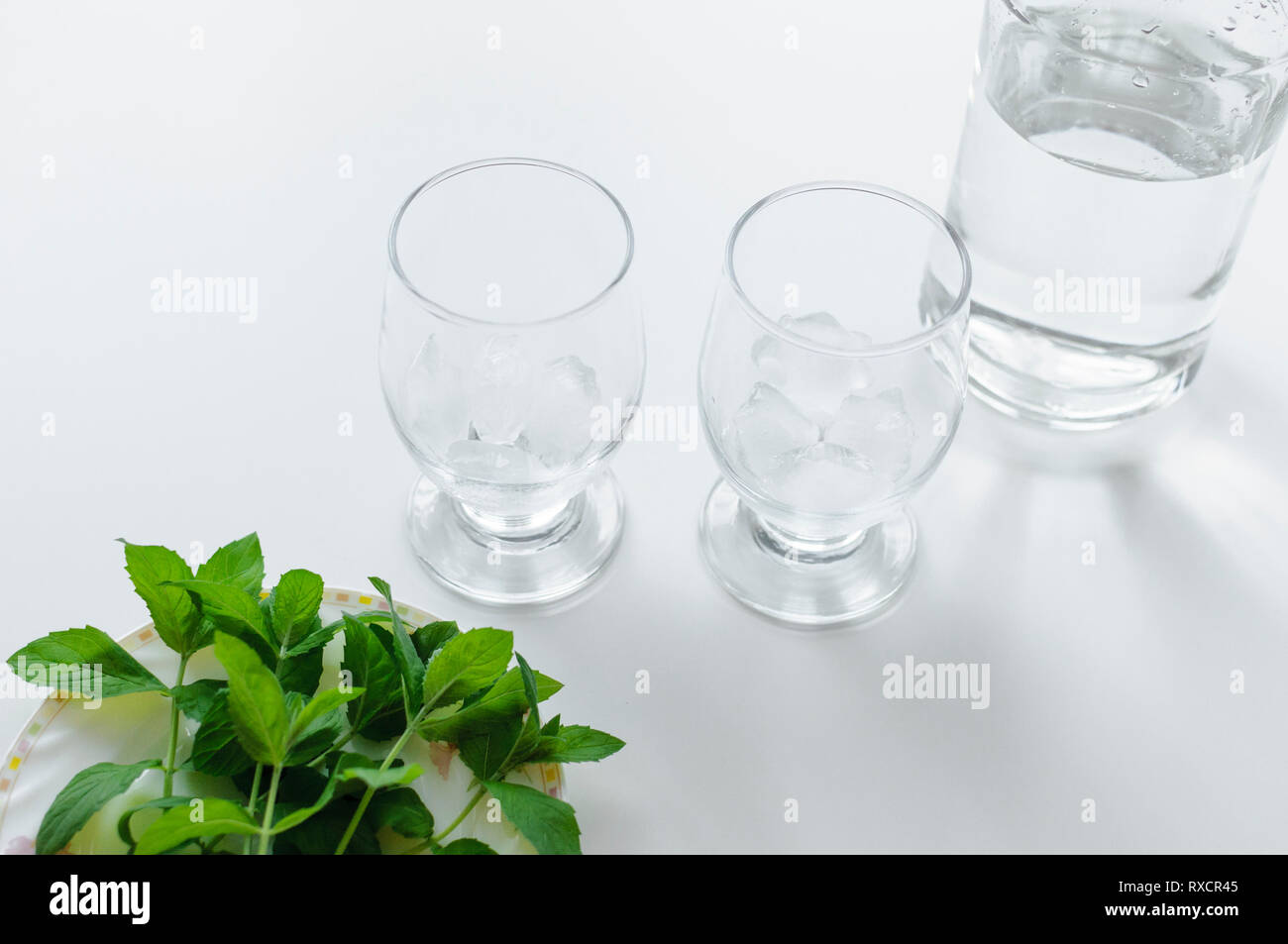 Deux verres avec des cubes de glace, bouteille d'eau et de menthe verte fraîche sur une assiette. Banque D'Images