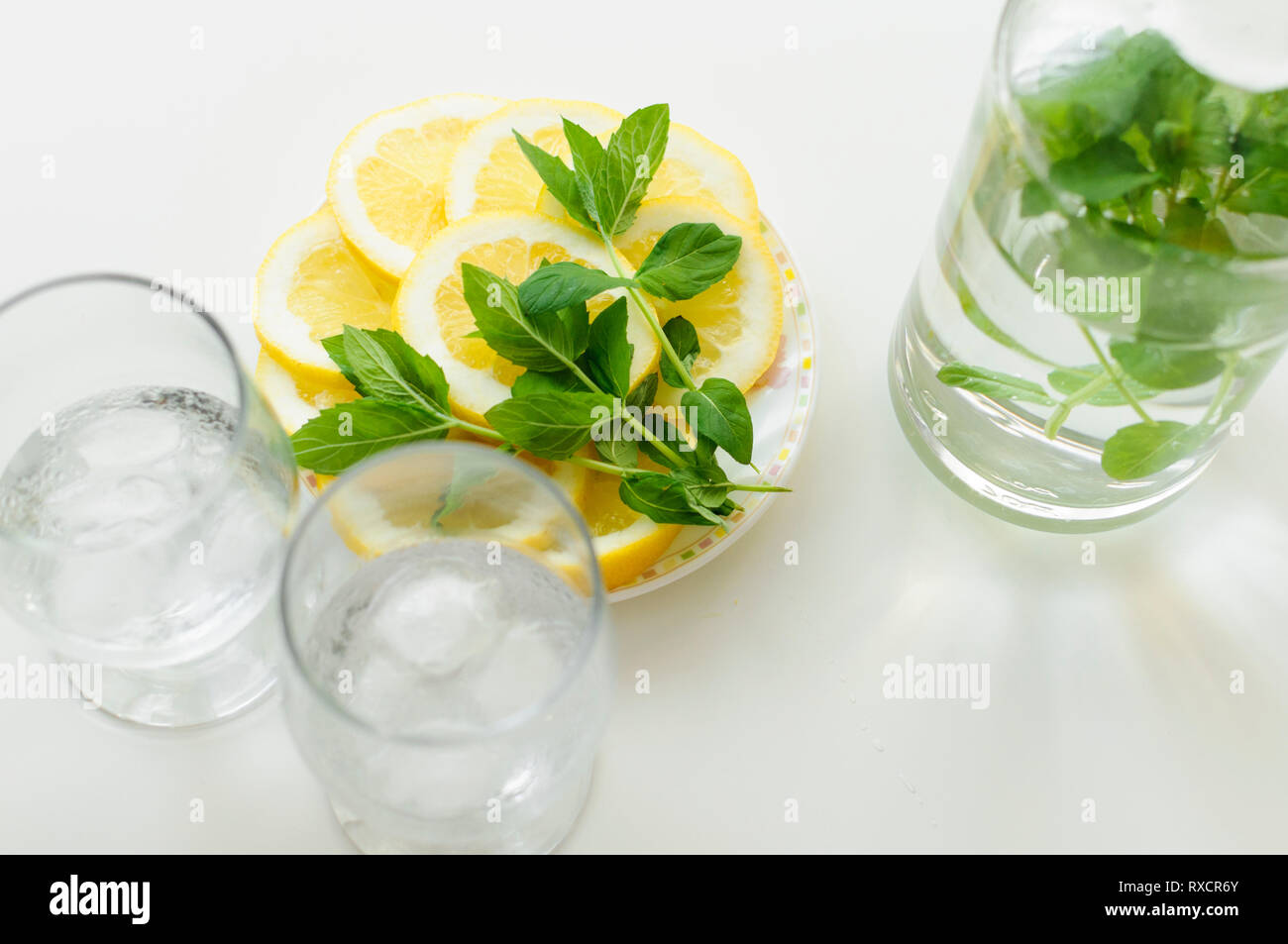 Vue de dessus de deux verres avec des cubes de glace, la plaque avec les tranches de citron et de feuilles de menthe et aussi une bouteille d'eau, le tout sur le tableau blanc. Banque D'Images