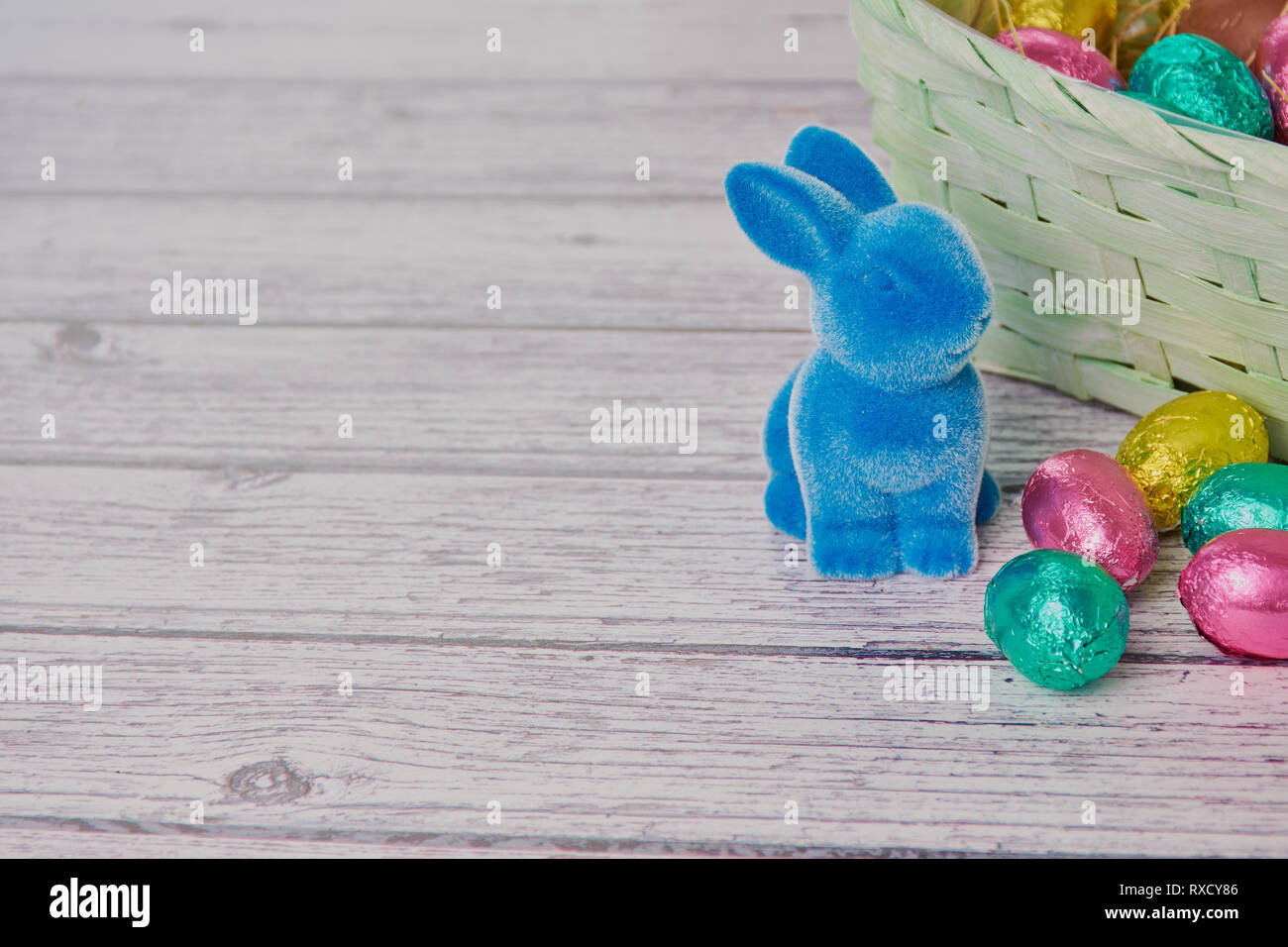 Lapin de Pâques bleu à côté des œufs en chocolat, de couleur en arrière-plan un panier de Pâques sur fond de bois blanc Banque D'Images