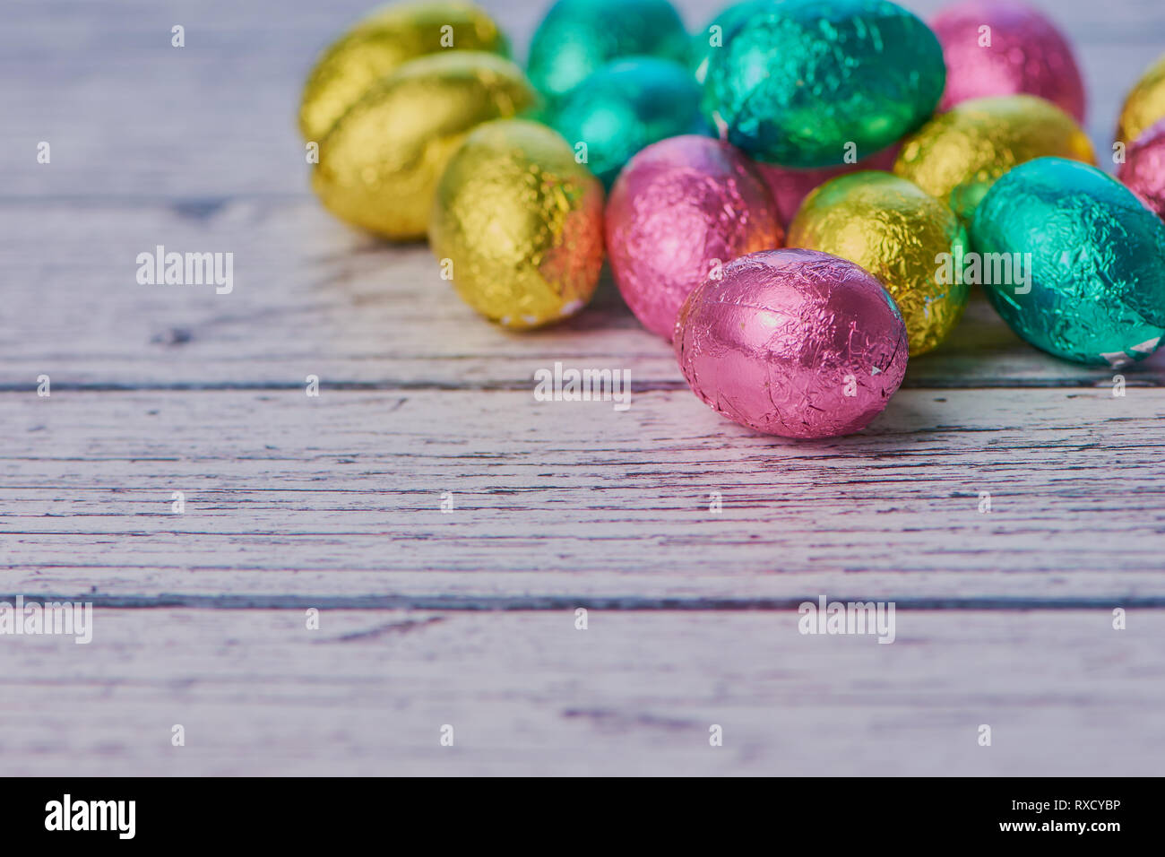 Les œufs en chocolat coloré enroulé contre l'arrière-plan en bois blanc avec copie espace, macro photo couleur Banque D'Images