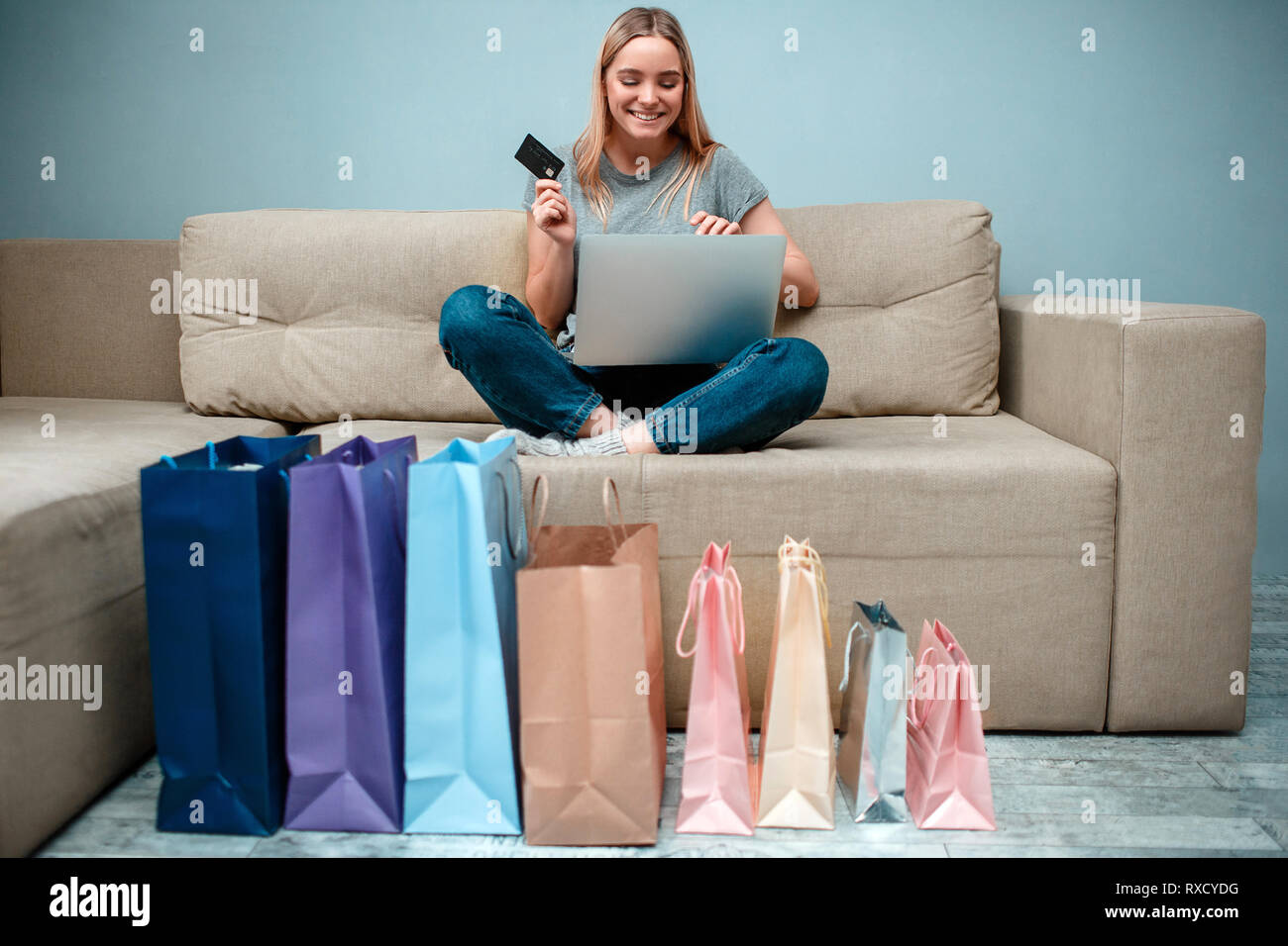 Magasinage en ligne à la maison. Jeune femme heureuse avec carte de crédit  est prête à beaucoup de ventes en magasin en ligne tout en restant assis  sur le canapé avec shopping