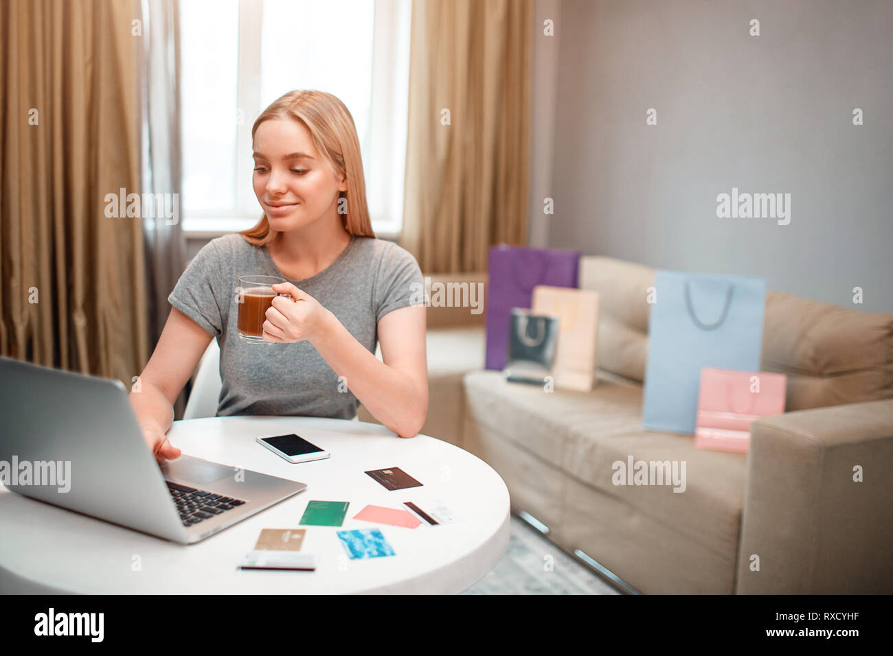 Magasinage en ligne à la maison. Jeune blonde shopper avec plateau est heureux de gros rabais de vendredi noir alors qu'il était assis à la table Banque D'Images