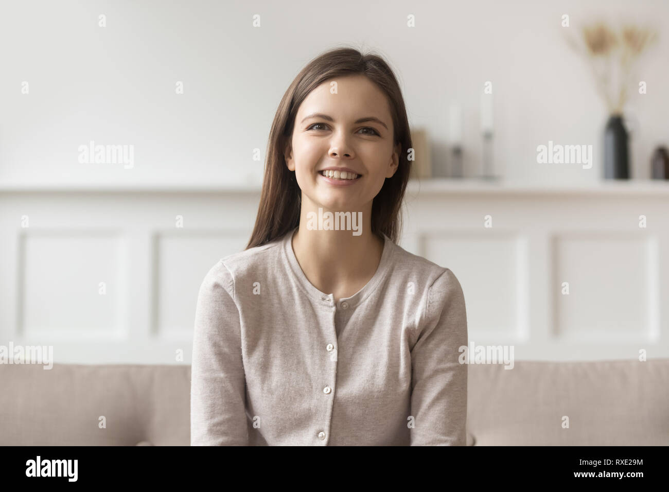 Smiling young casual woman sitting on couch looking at camera Banque D'Images