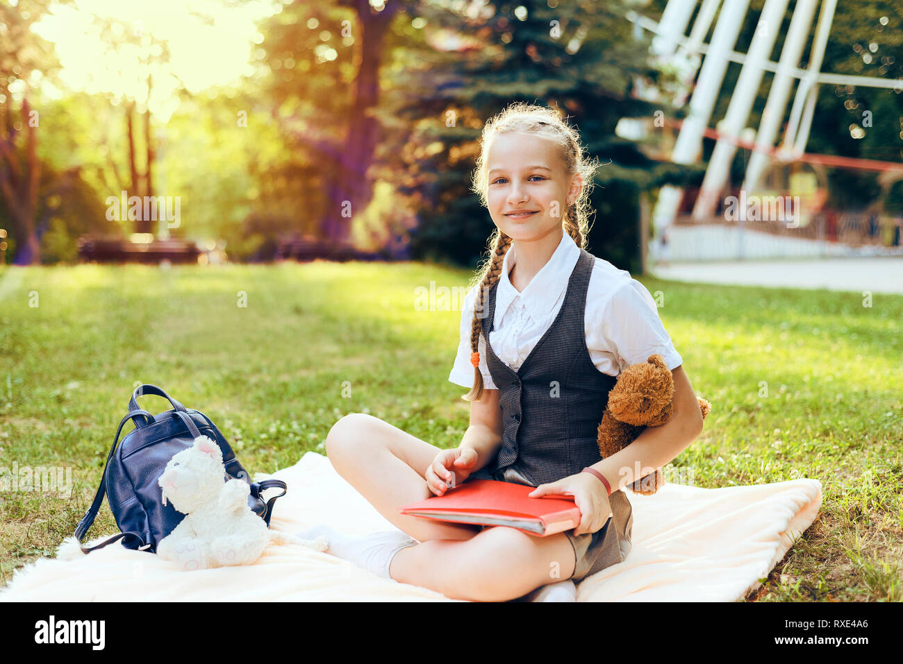 Portrait de la belle adolescente lycéenne en uniforme avec des nattes, des livres et d'ordinateurs portables. femme enfant sourit, est titulaire d'un soft toy ours au coucher du soleil dans le su Banque D'Images