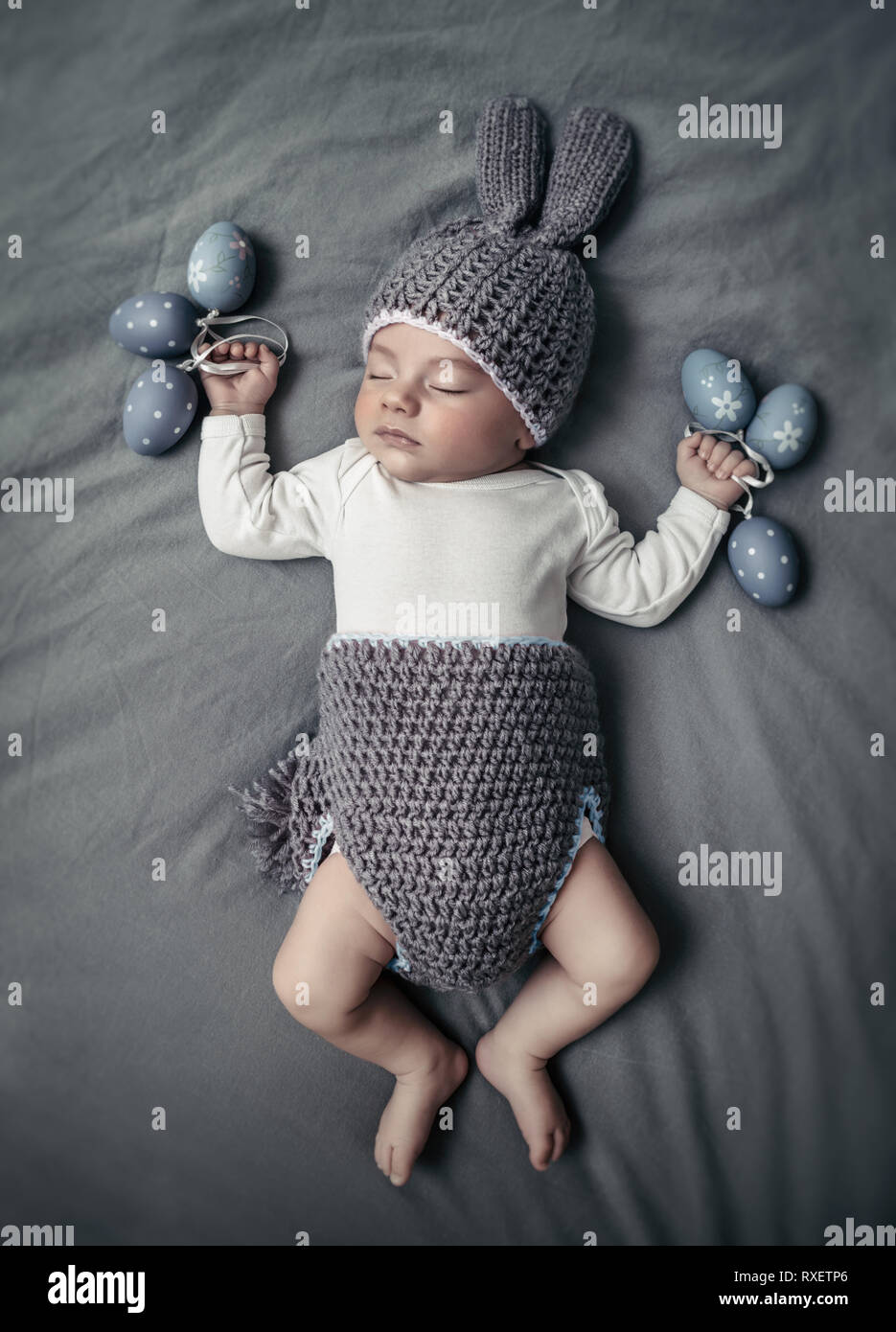 Mignon petit bébé habillé comme un lapin de Pâques, adorable garçon nouveau-né de dormir sur la couverture grise avec arrière-plan gris élégant décoré des oeufs de Pâques, h Banque D'Images